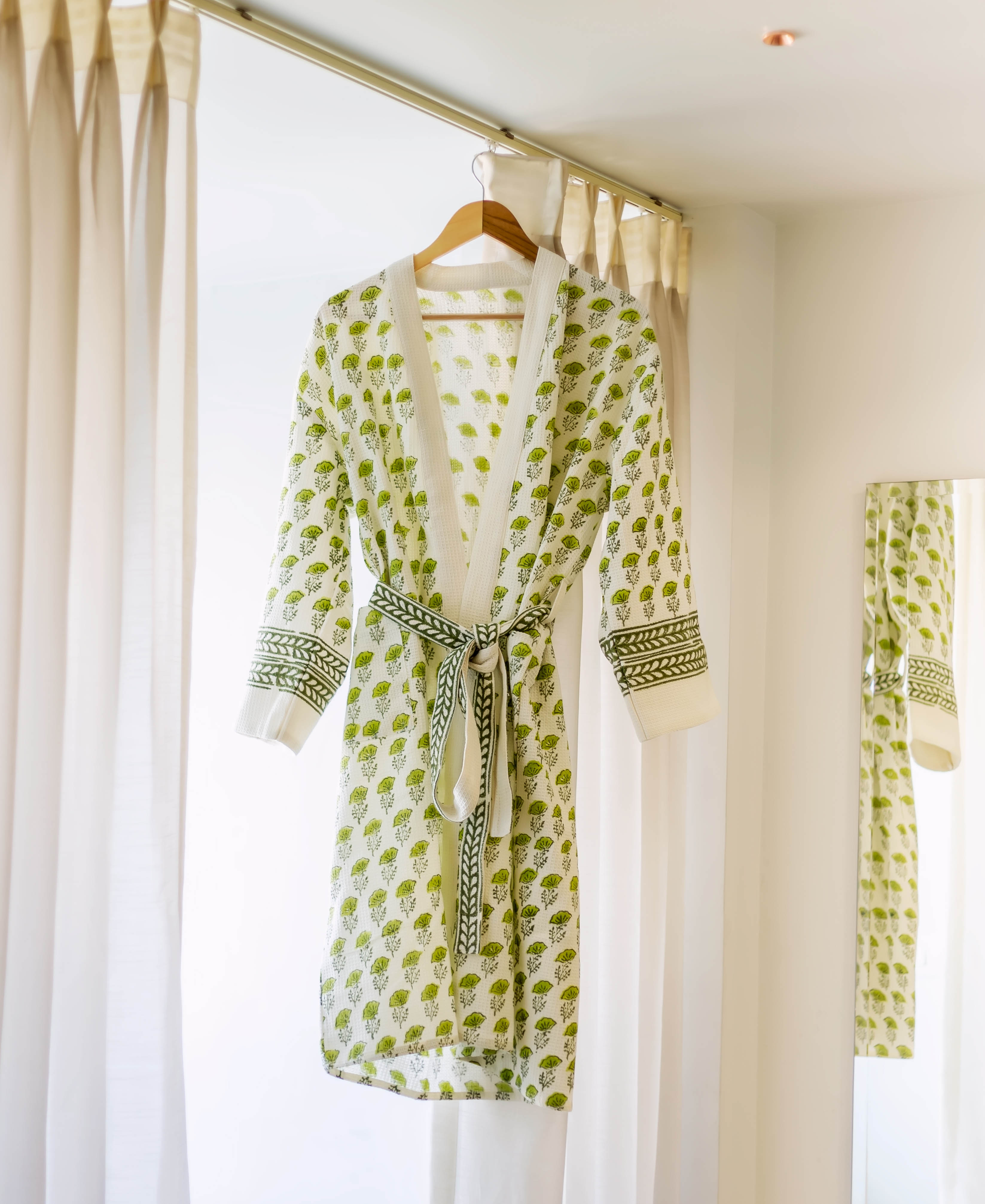 A white bath robe with green floral print and a matching belt, hanging from a wooden hanger.