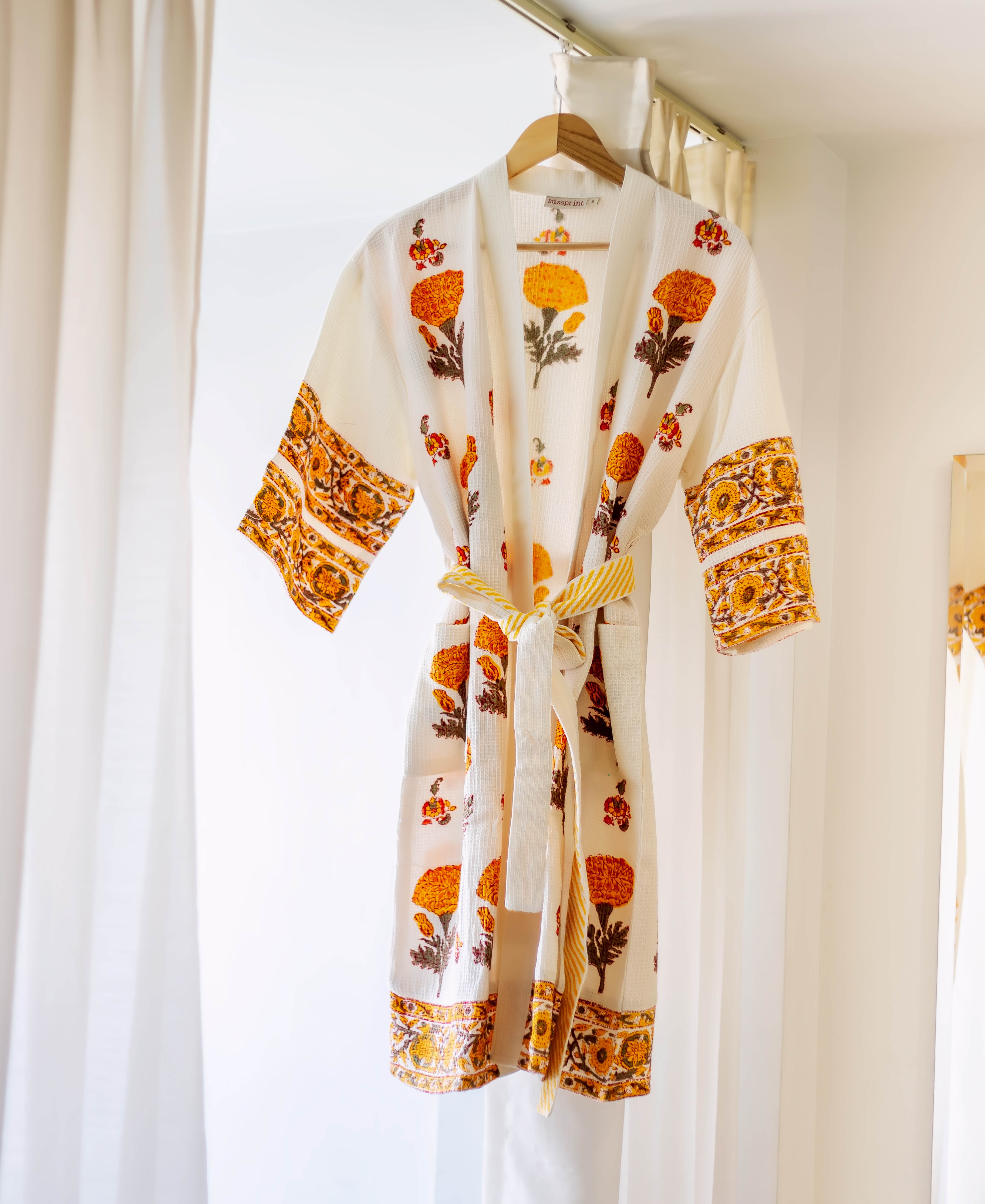 Hand block printed cream waffle robe with vibrant orange marigold flowers and yellow borders, hanging.