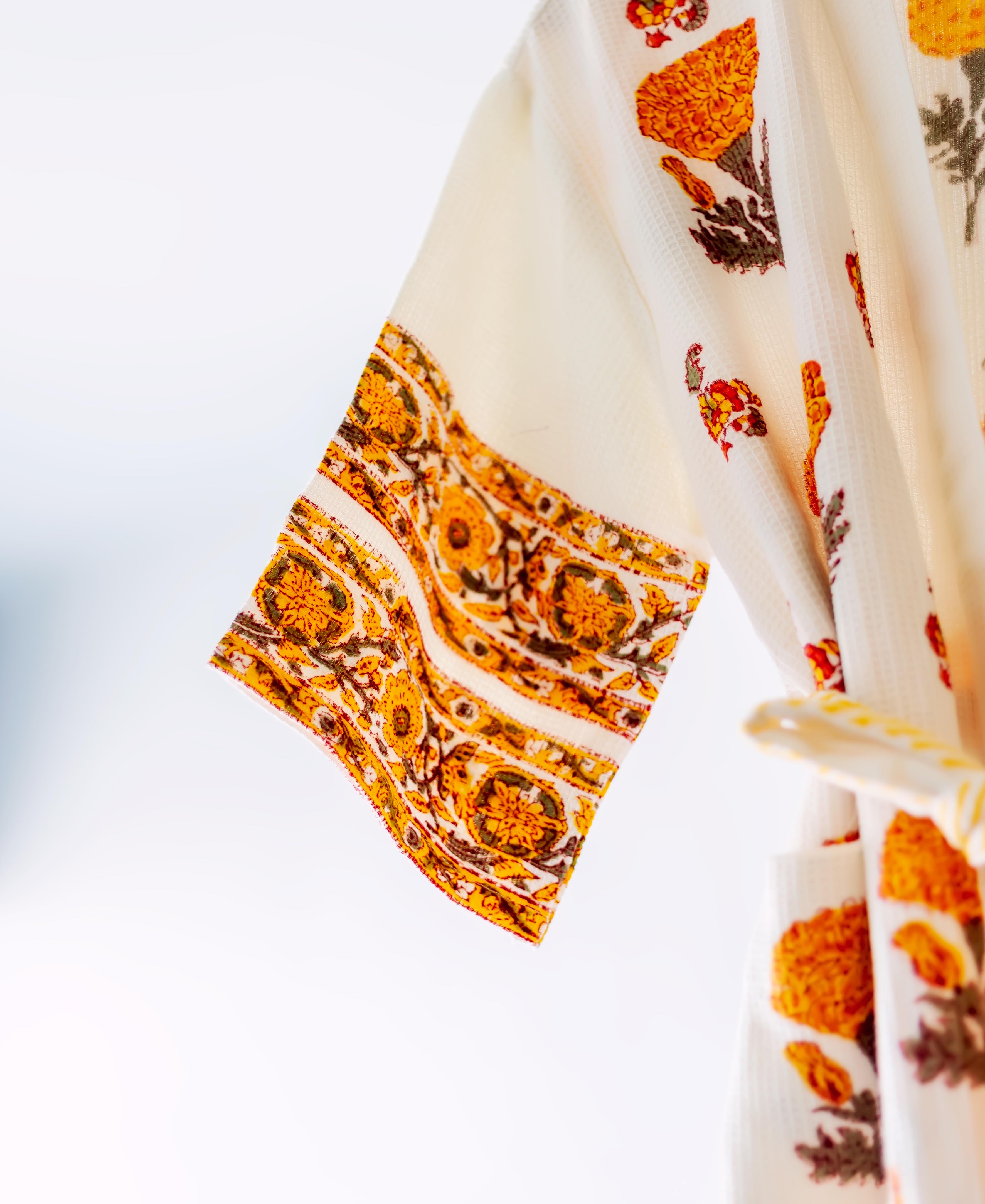 Close-up of hanging cream waffle robe sleeve, orange marigold hand-block floral and ethnic prints.