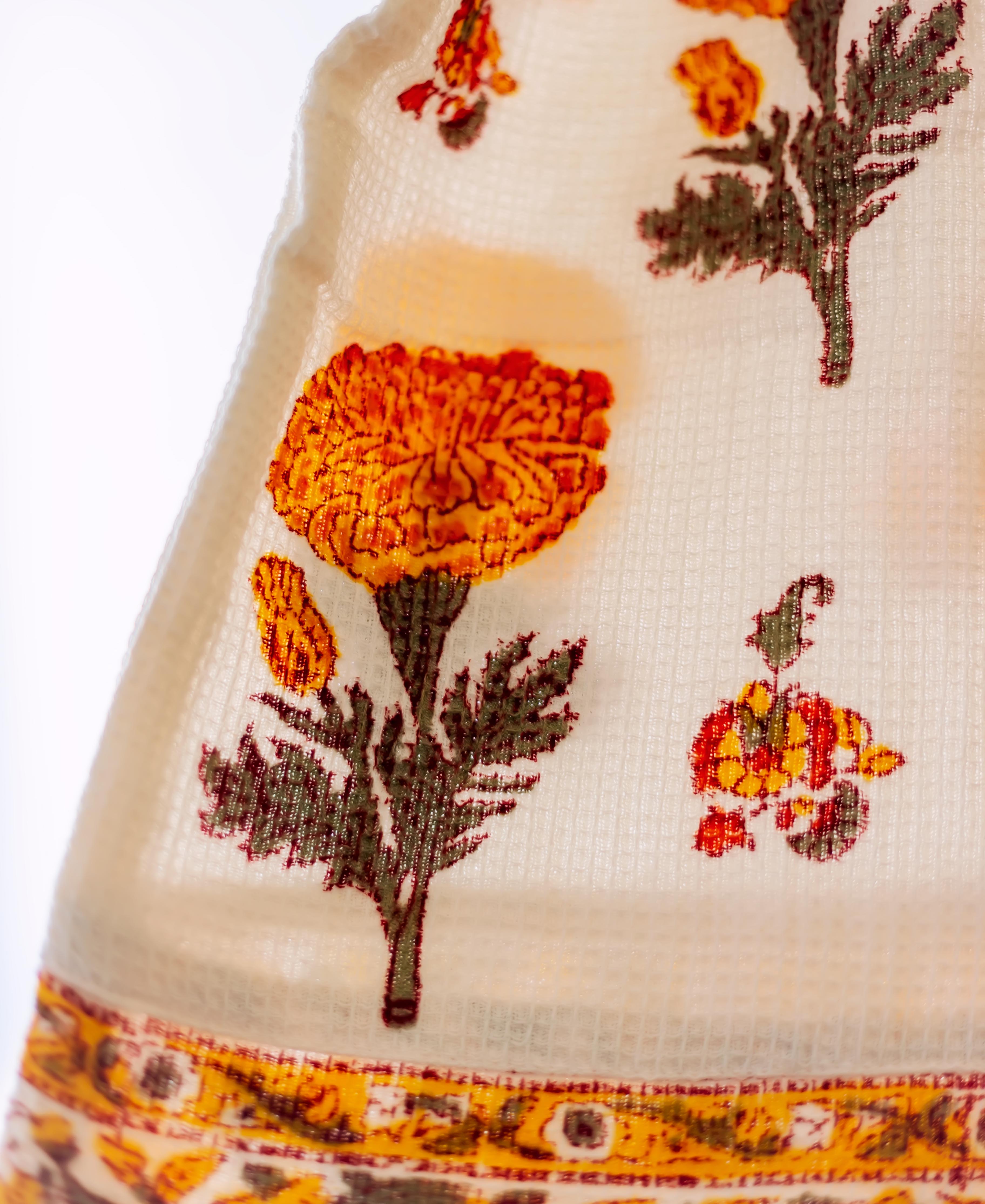 A close-up of a white bath robe with marigold floral print and yellow border.