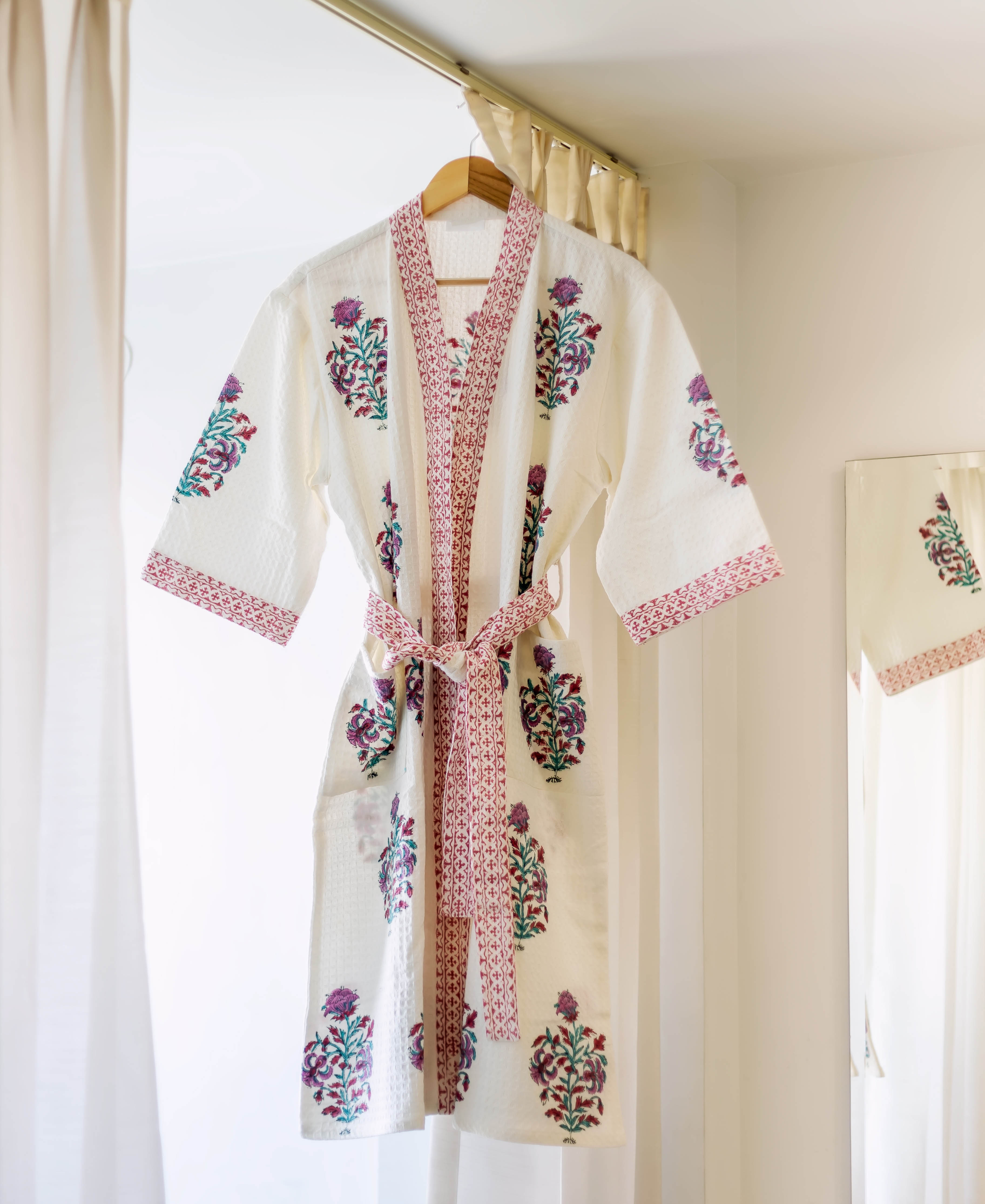 White hand-block printed bath robe with purple, green floral buti and magenta trim, hanging.