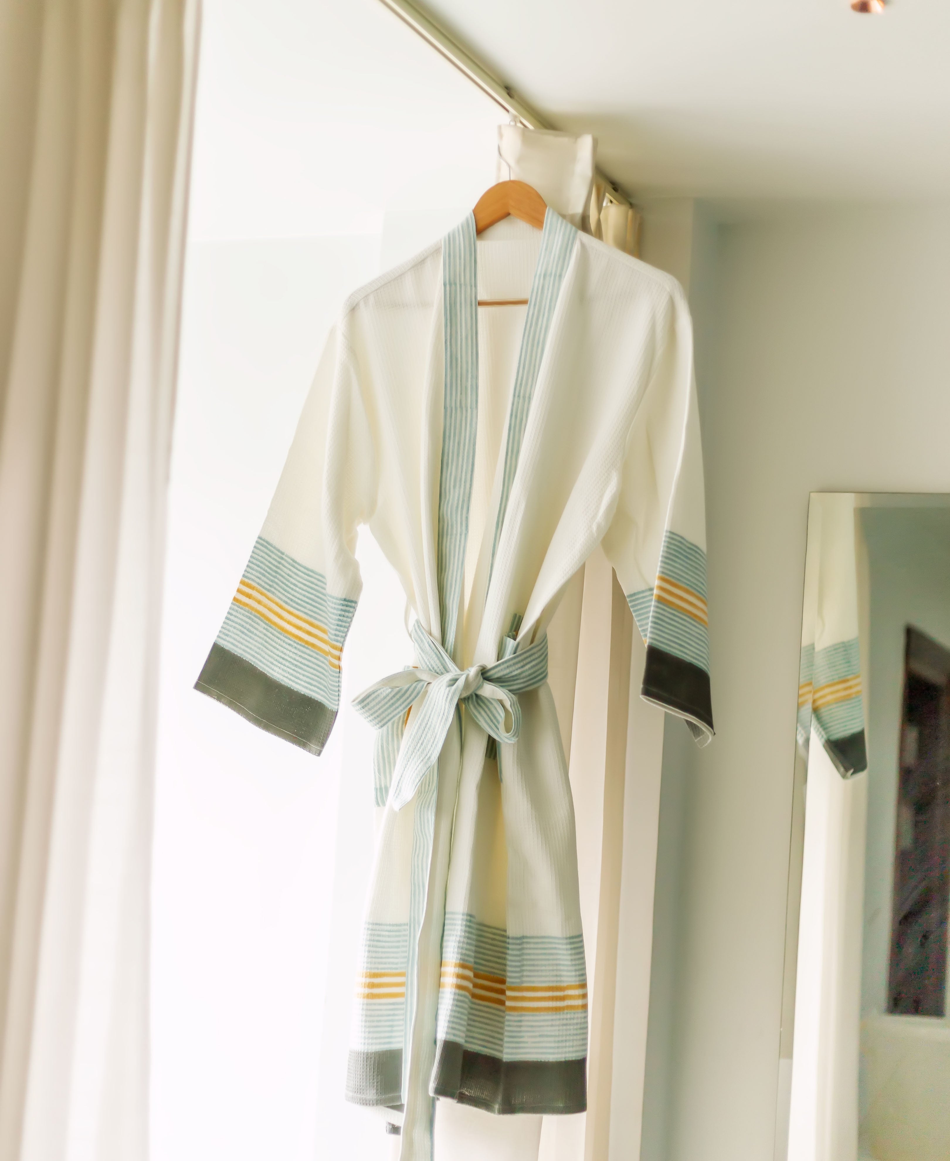White robe with pastel blue, yellow, and dark grey stripes on sleeves and hem, tied at waist.