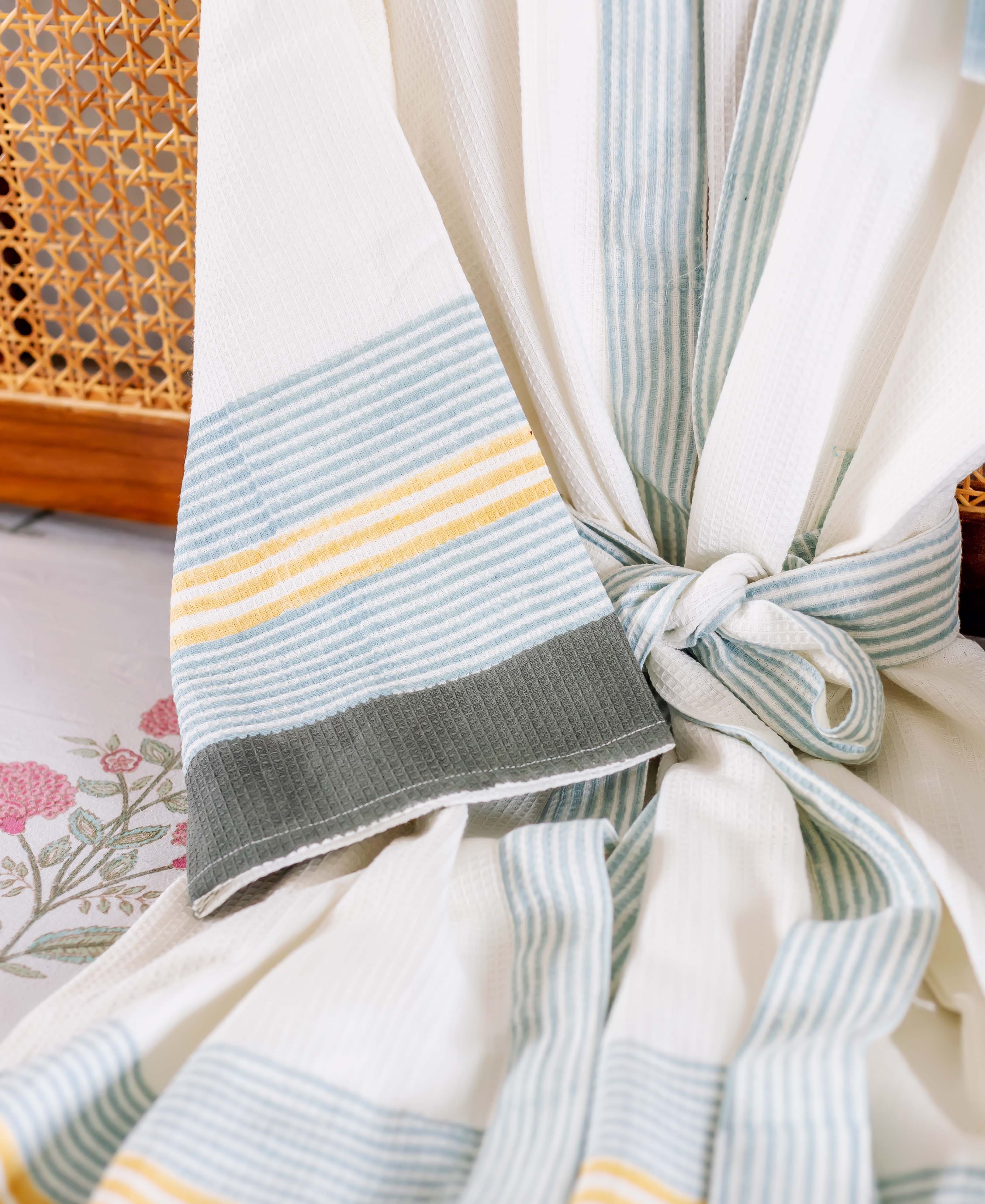 Close-up of a white waffle robe with aqua, yellow, and grey striped cuff and tied waist.
