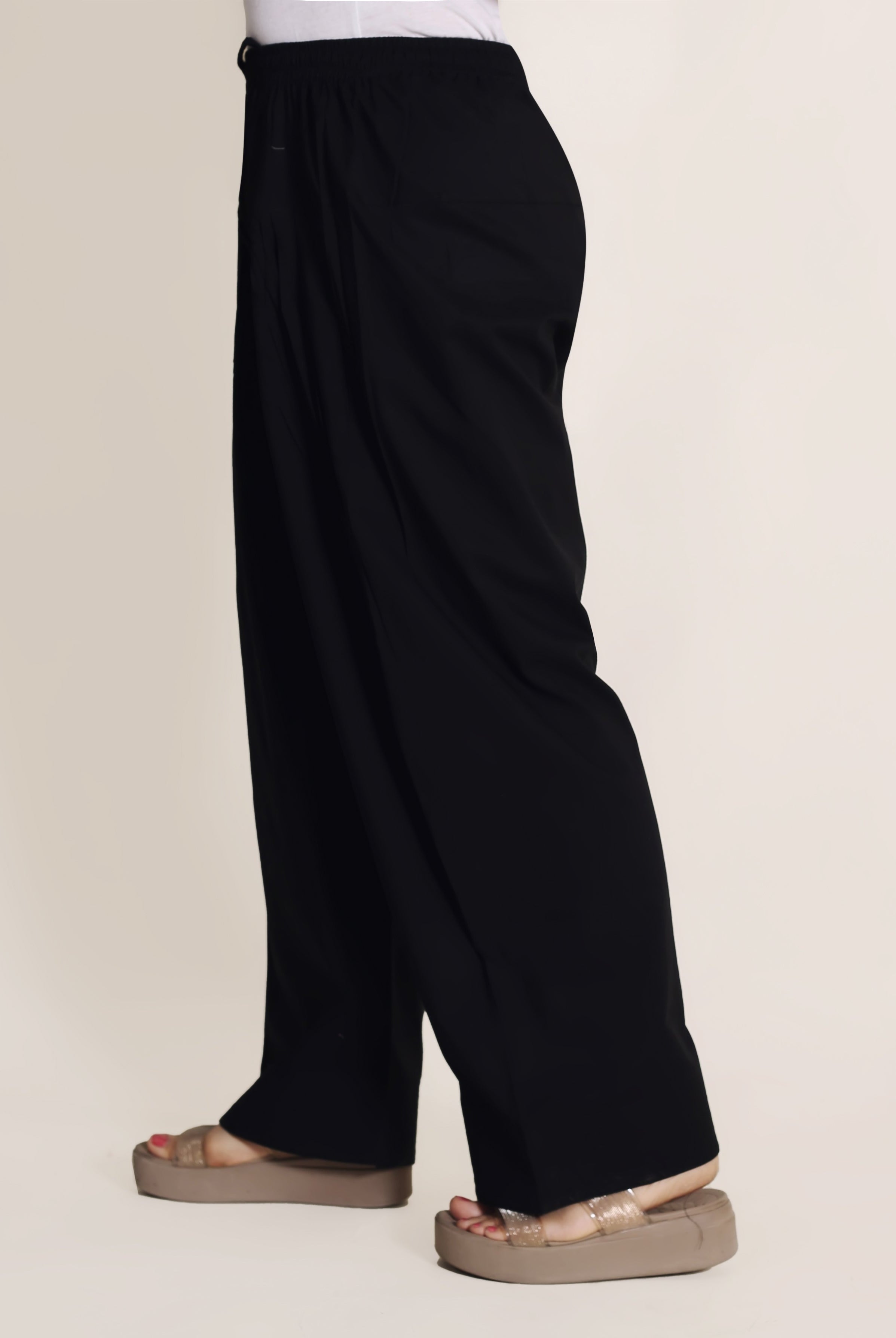 Side view of model wearing loose-fitting solid black farshi salwar with a drawstring.