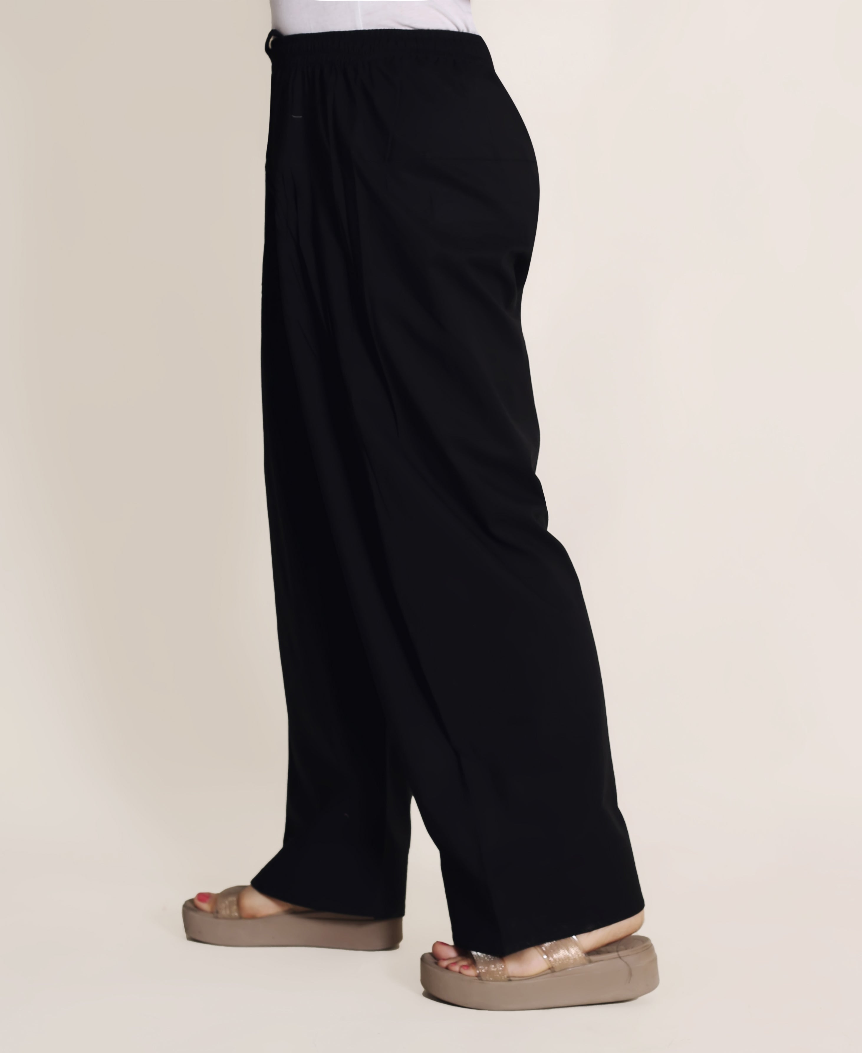 Side view of model wearing loose-fitting solid black farshi salwar with a drawstring.