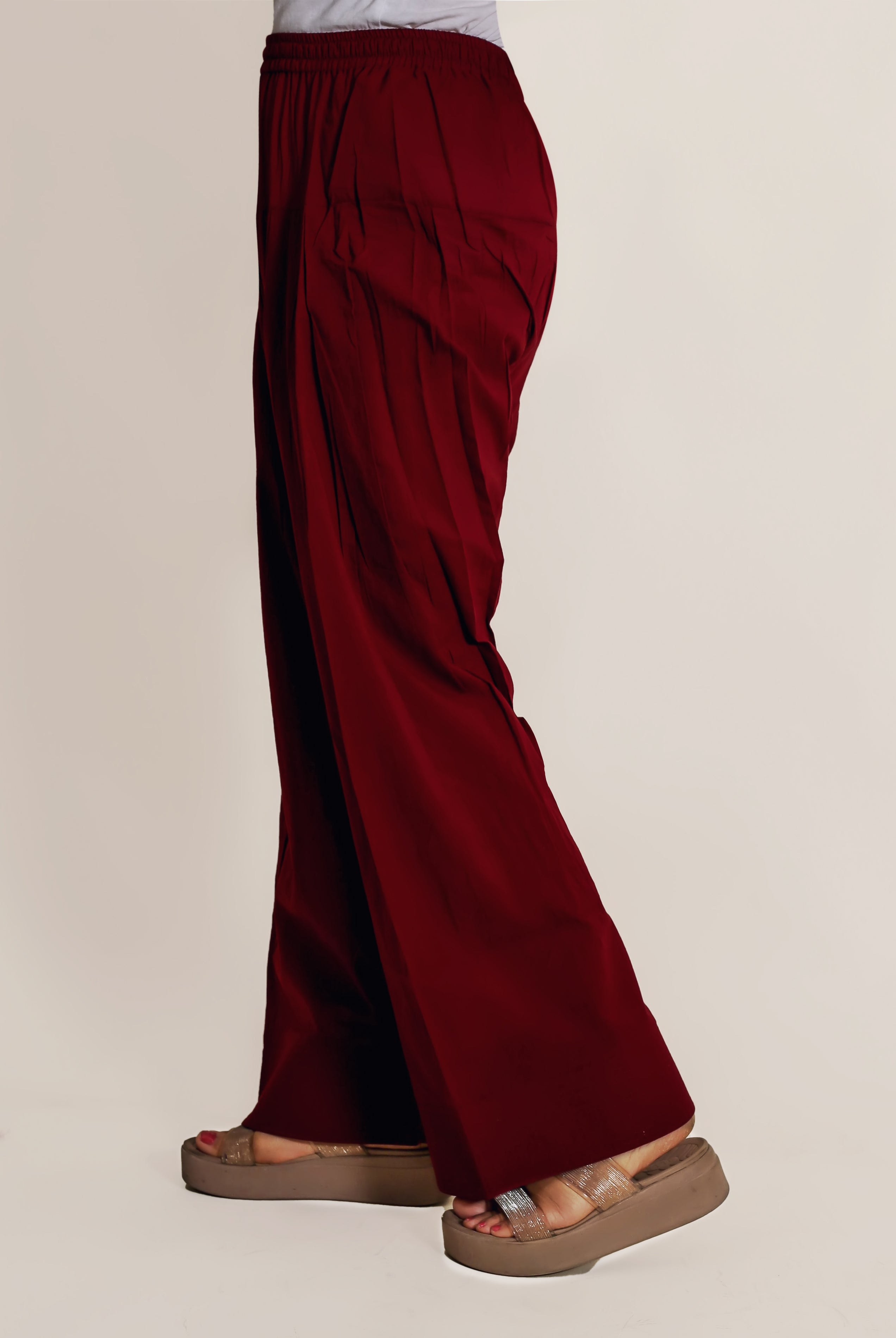 A model's lower body wearing maroon farshi salwar with a white top and brown sandals.
