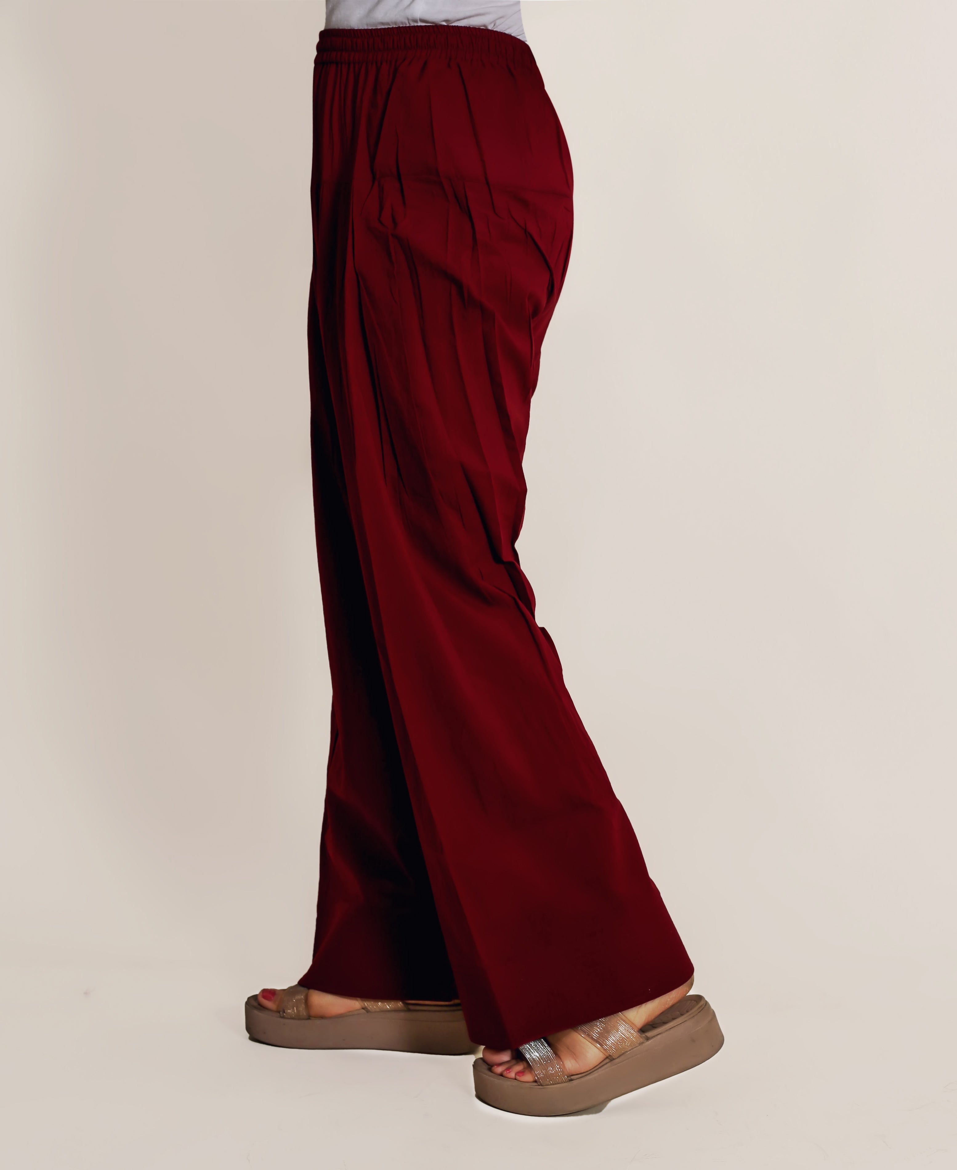 A model's lower body wearing maroon farshi salwar with a white top and brown sandals.