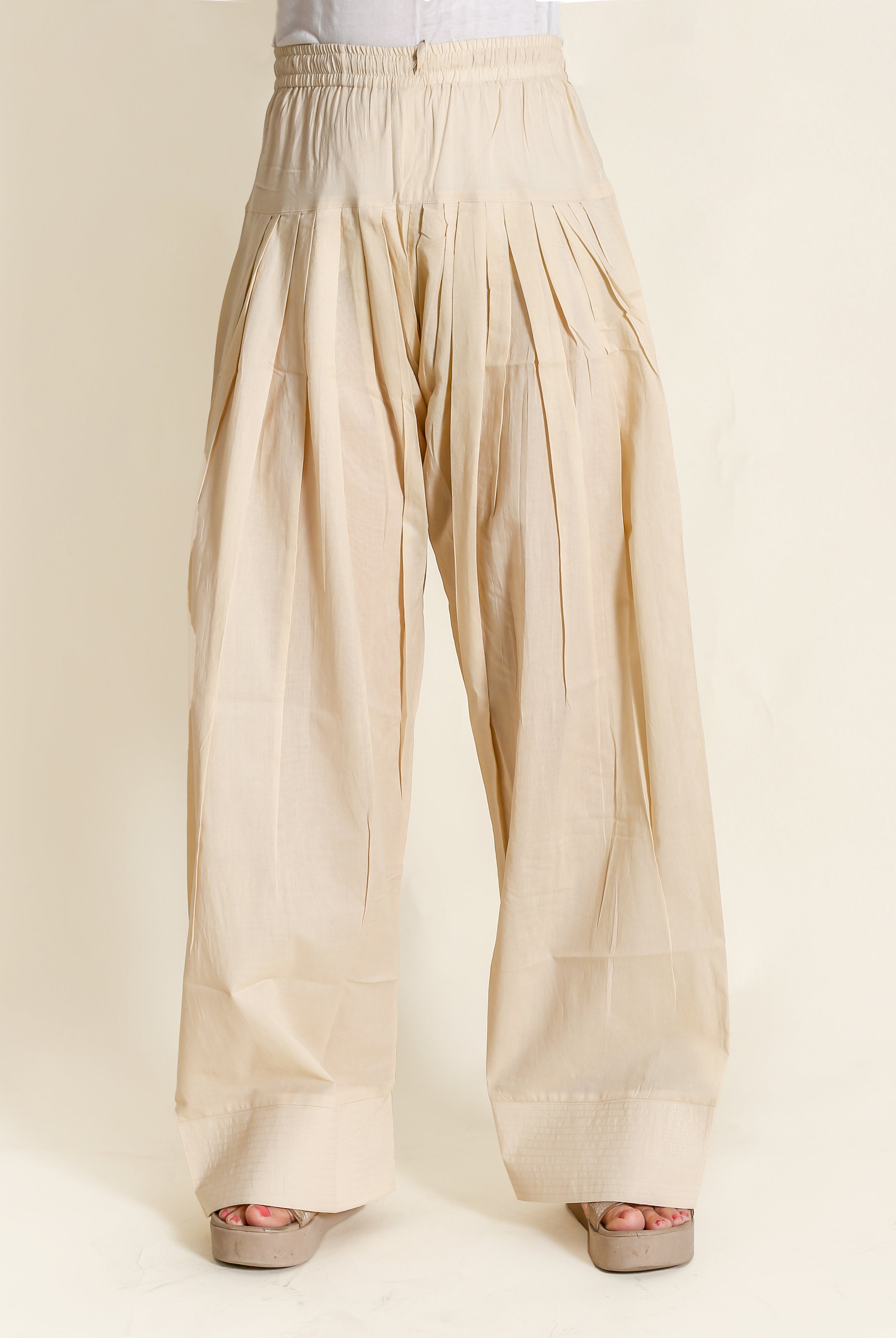 Beige wide-legged pants with pleats and elastic waistband on a model with tan heels.