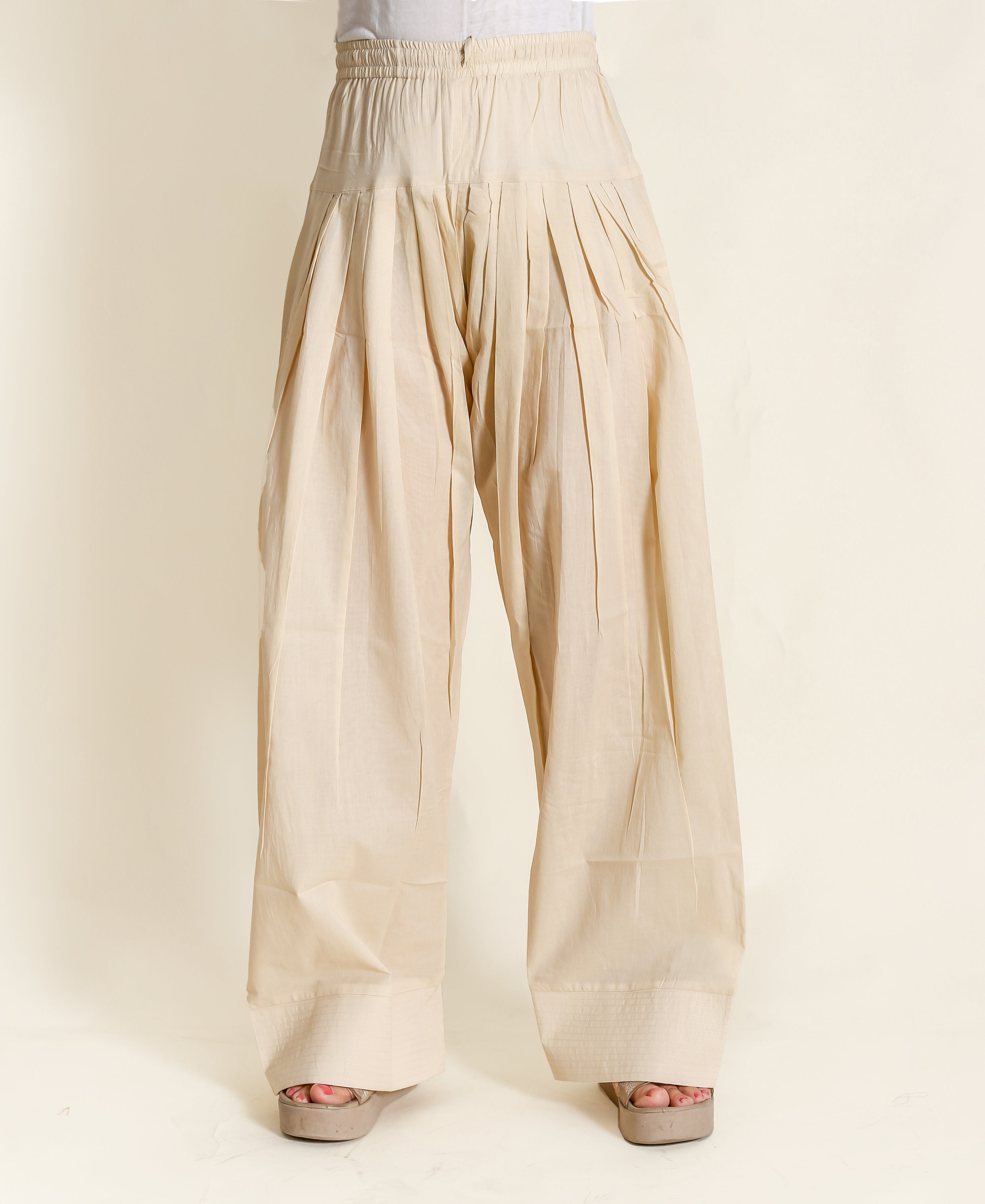 Beige wide-legged pants with pleats and elastic waistband on a model with tan heels.