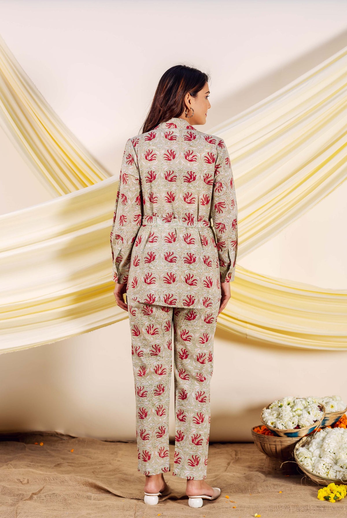 Model from back in a greige hand-block printed co-ord set with red motifs and belt.