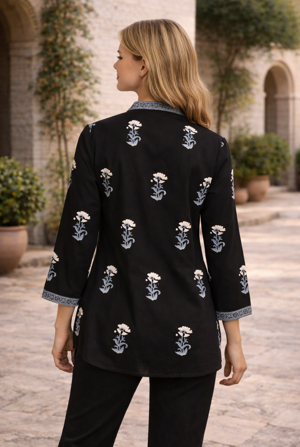 Black hand block printed top with white marigold flowers and blue leaves, model's back.