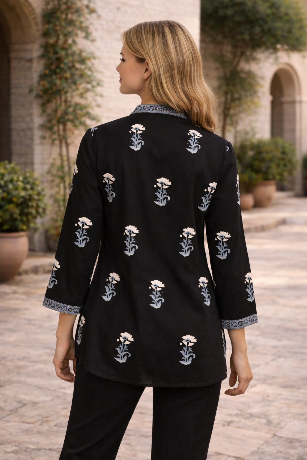Black hand block printed top with white marigold flowers and blue leaves, model's back.