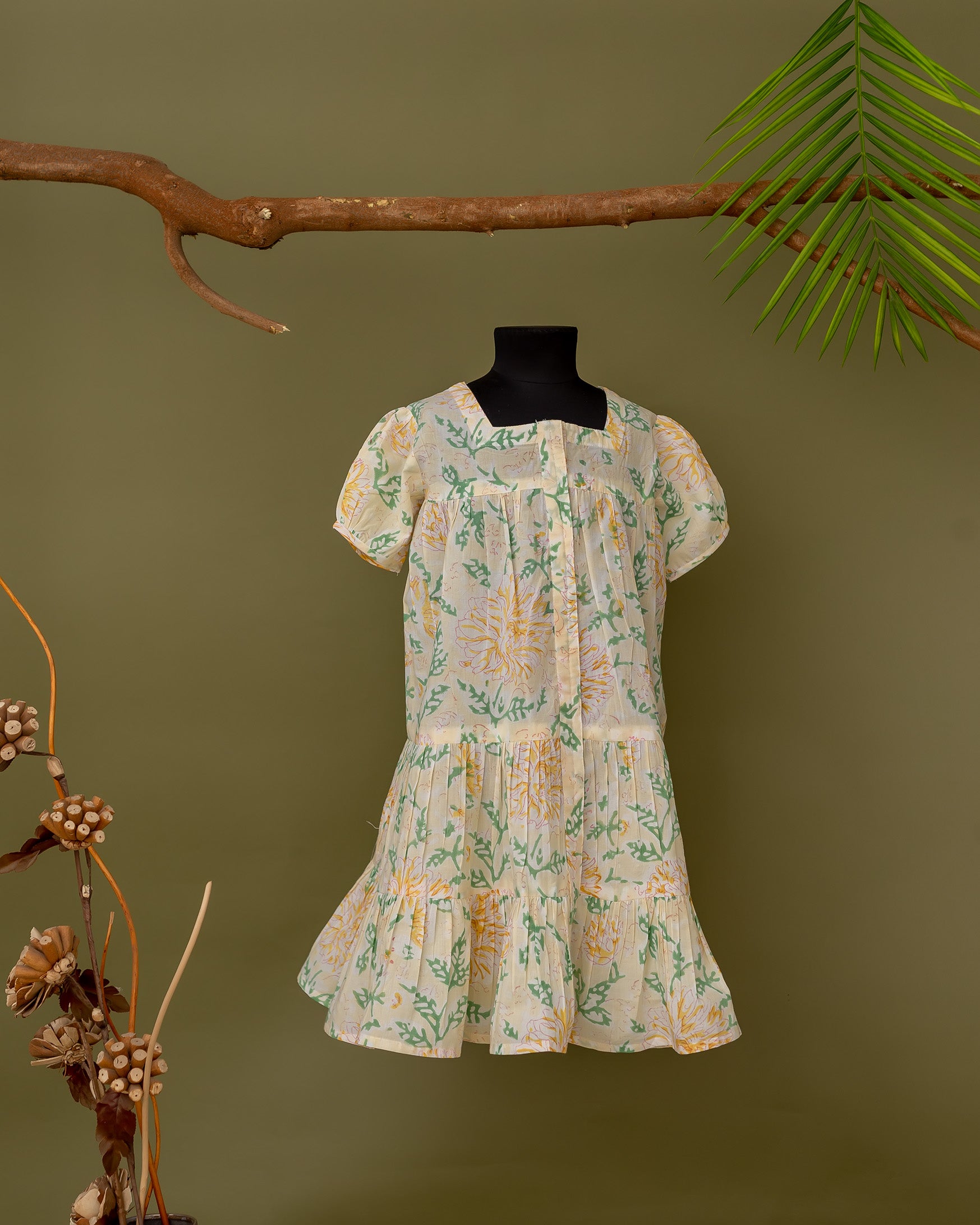 Front view cream baby dress on mannequin with square neck, green and yellow floral print.