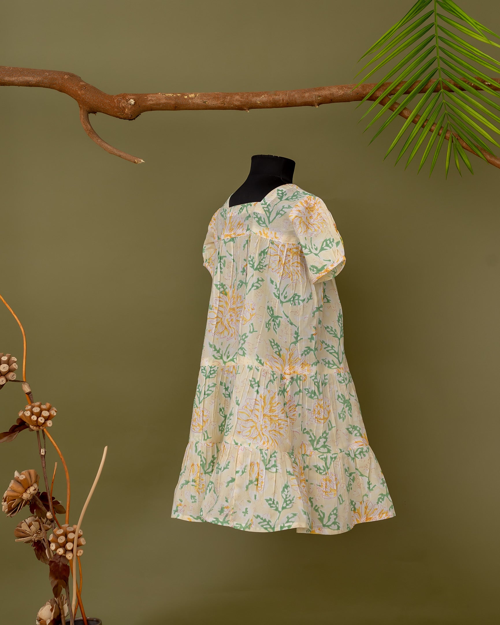 Yellow and green floral print baby girl dress on black mannequin, pleated short sleeves.