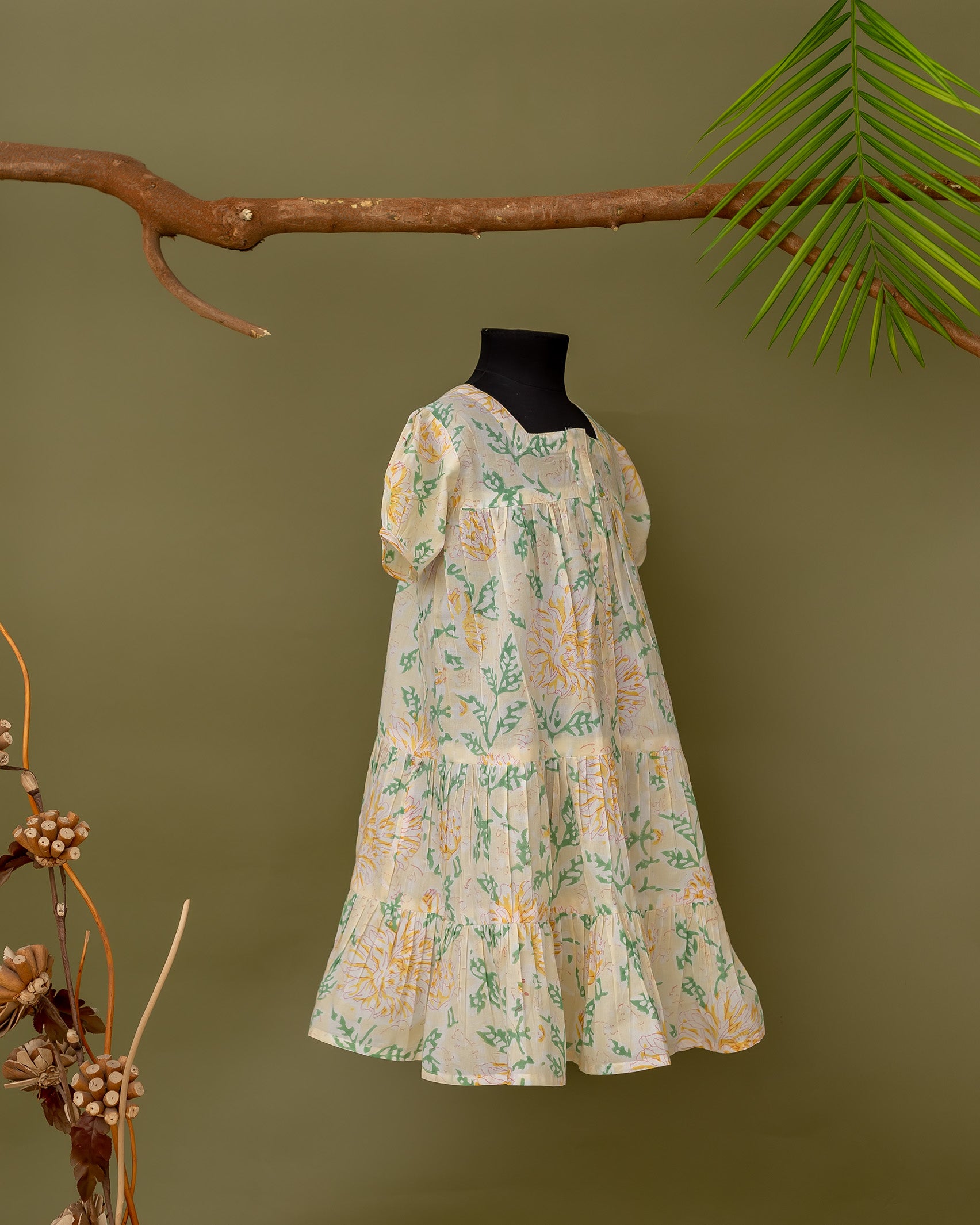 Mannequin side view of pale yellow baby girl's tiered dress with green and yellow floral print.