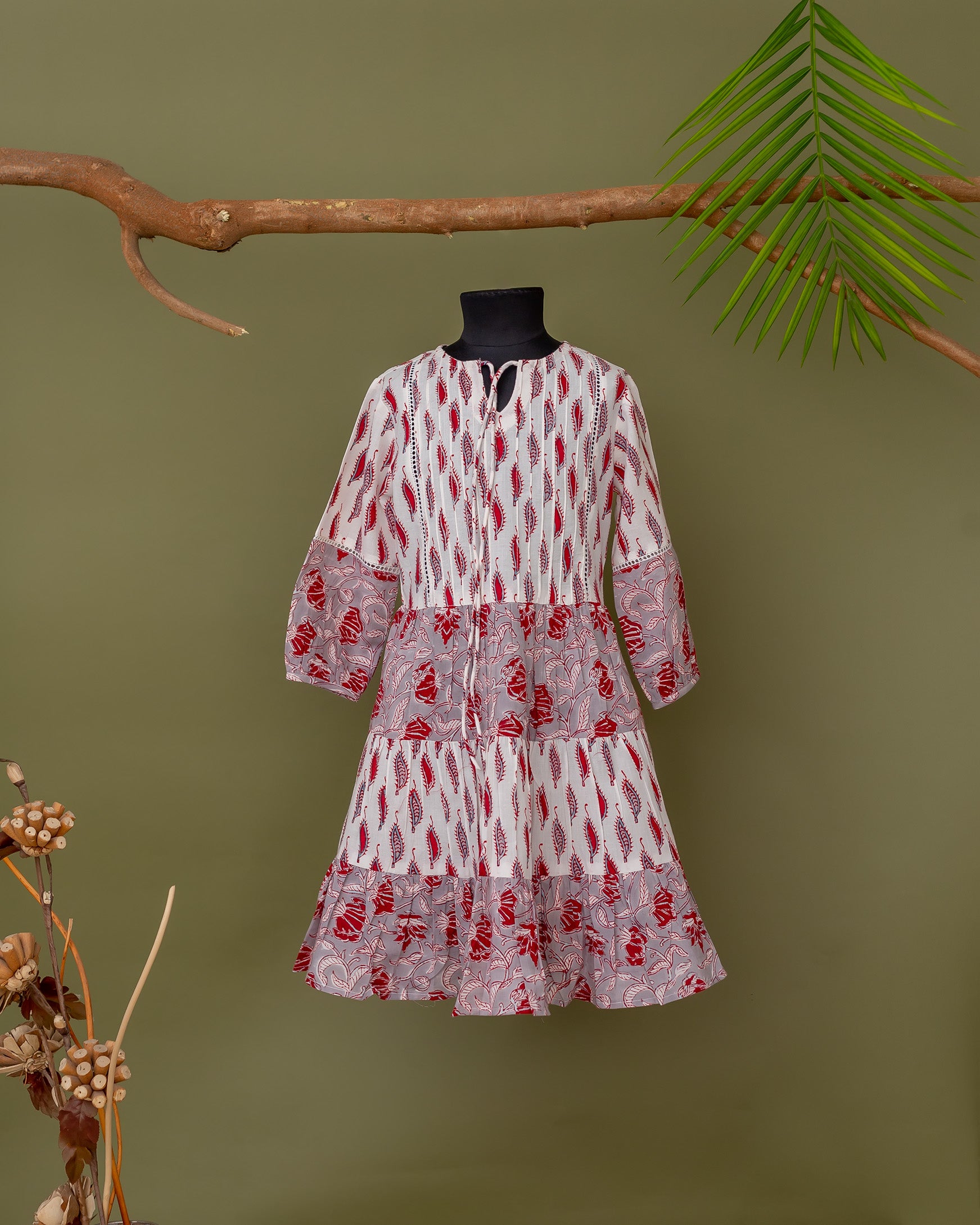 Front view hand-block printed tiered dress on mannequin, white with red feathers and grey-pink florals.