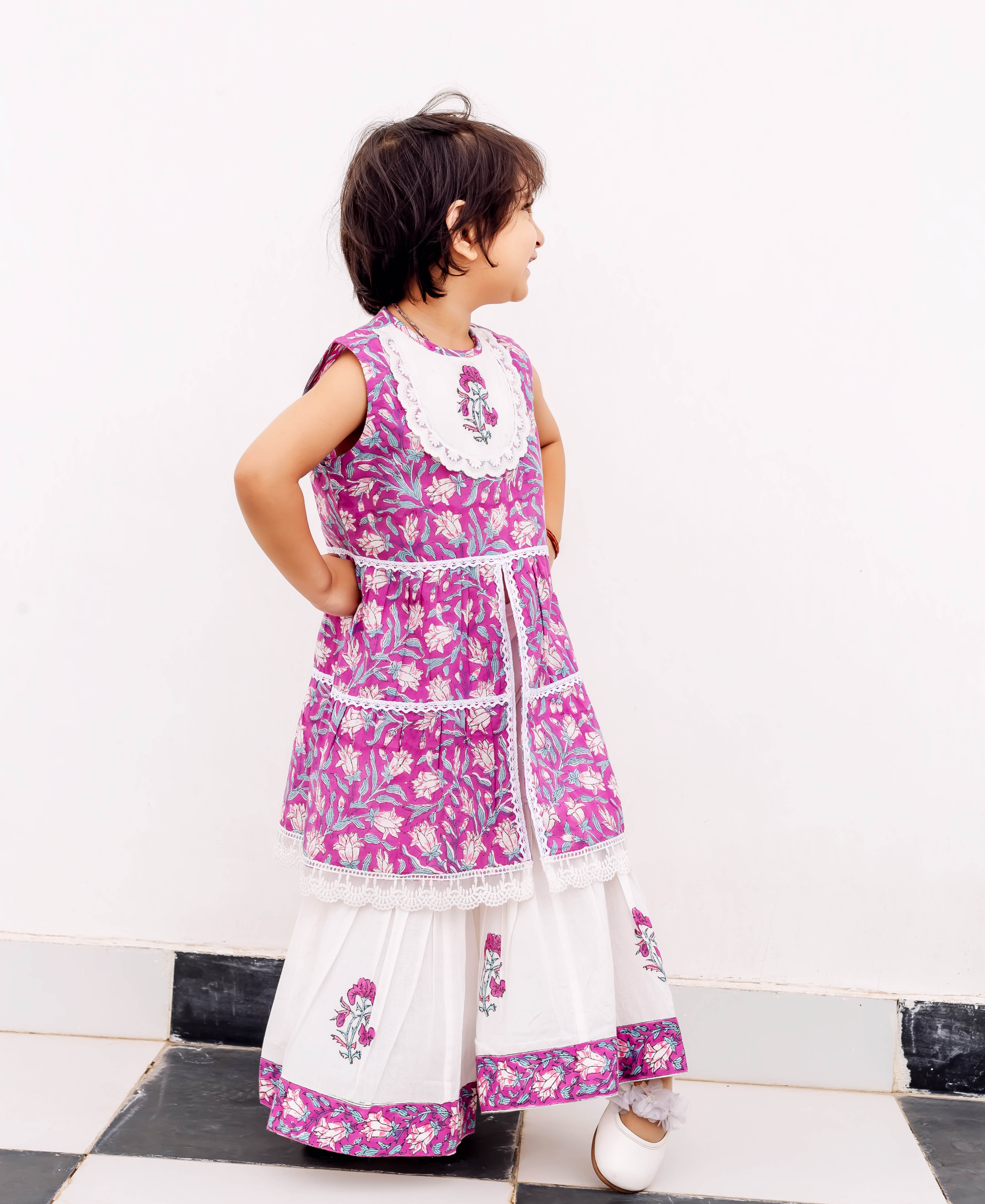 Young child in purple hand-block printed sleeveless kurta and white sharara, side profile.