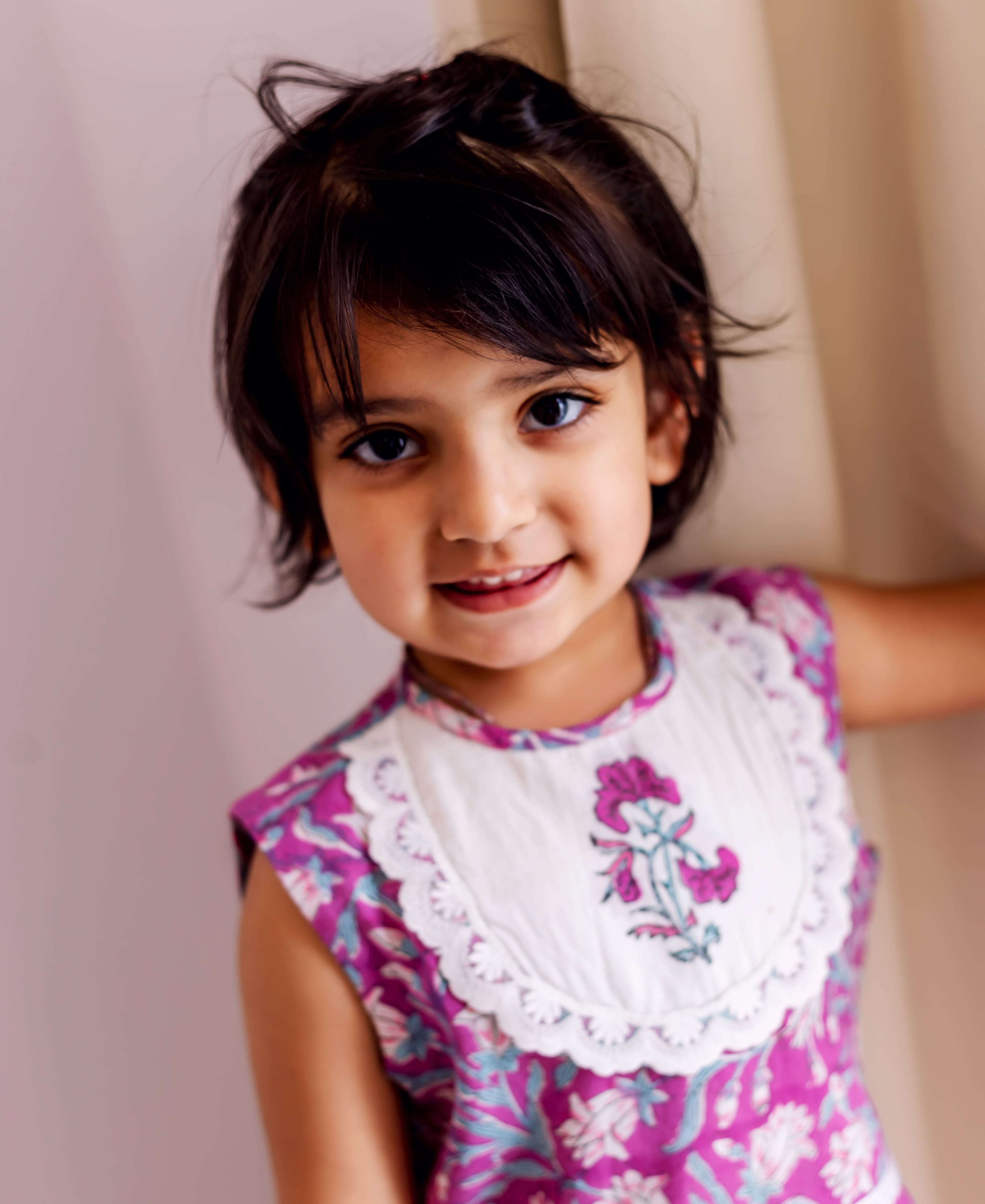 Smiling child model in purple hand block printed cotton kurta, with white scalloped floral bib.