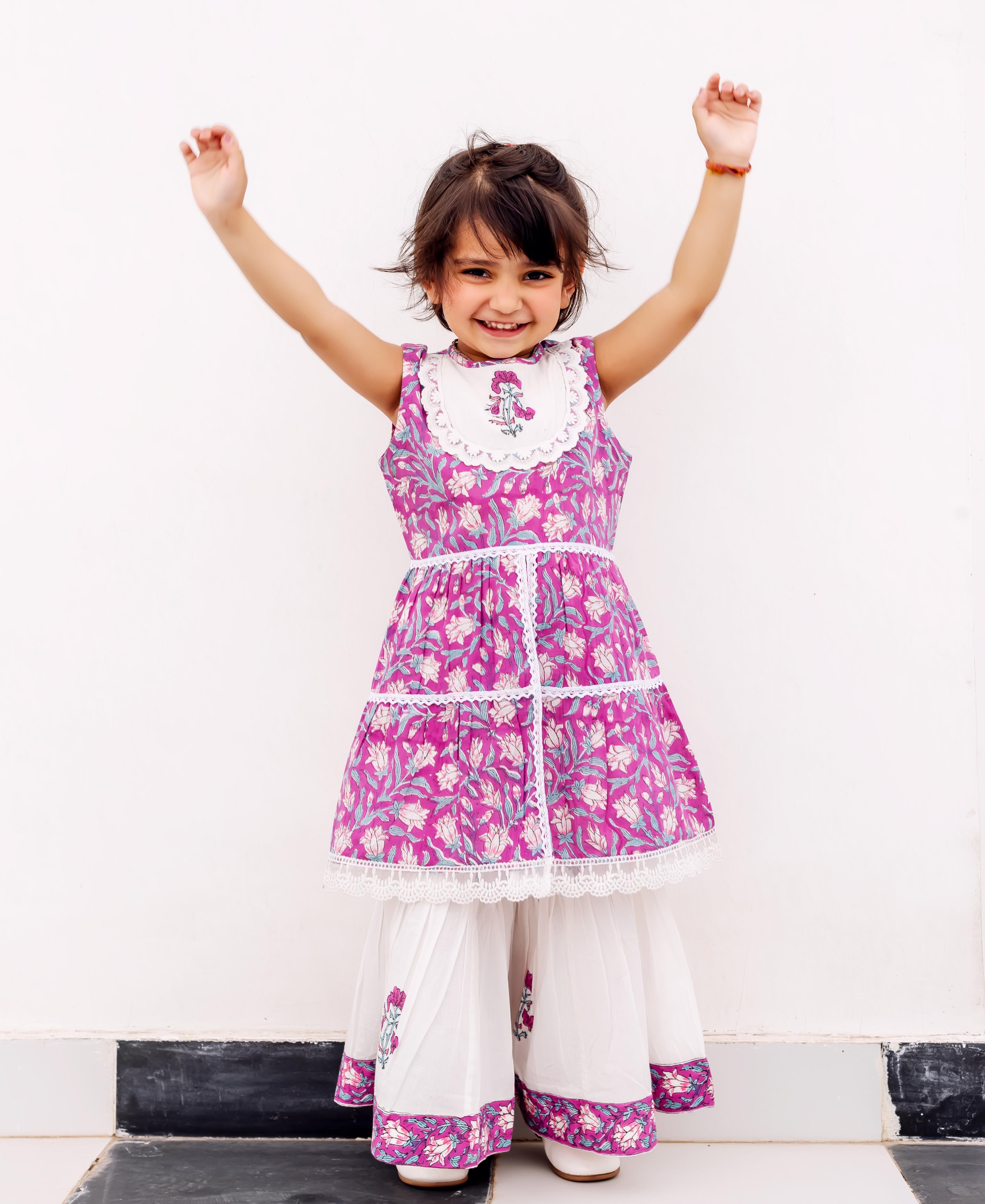 Young girl wearing a full purple hand-block printed cotton kurta with white floral sharara.