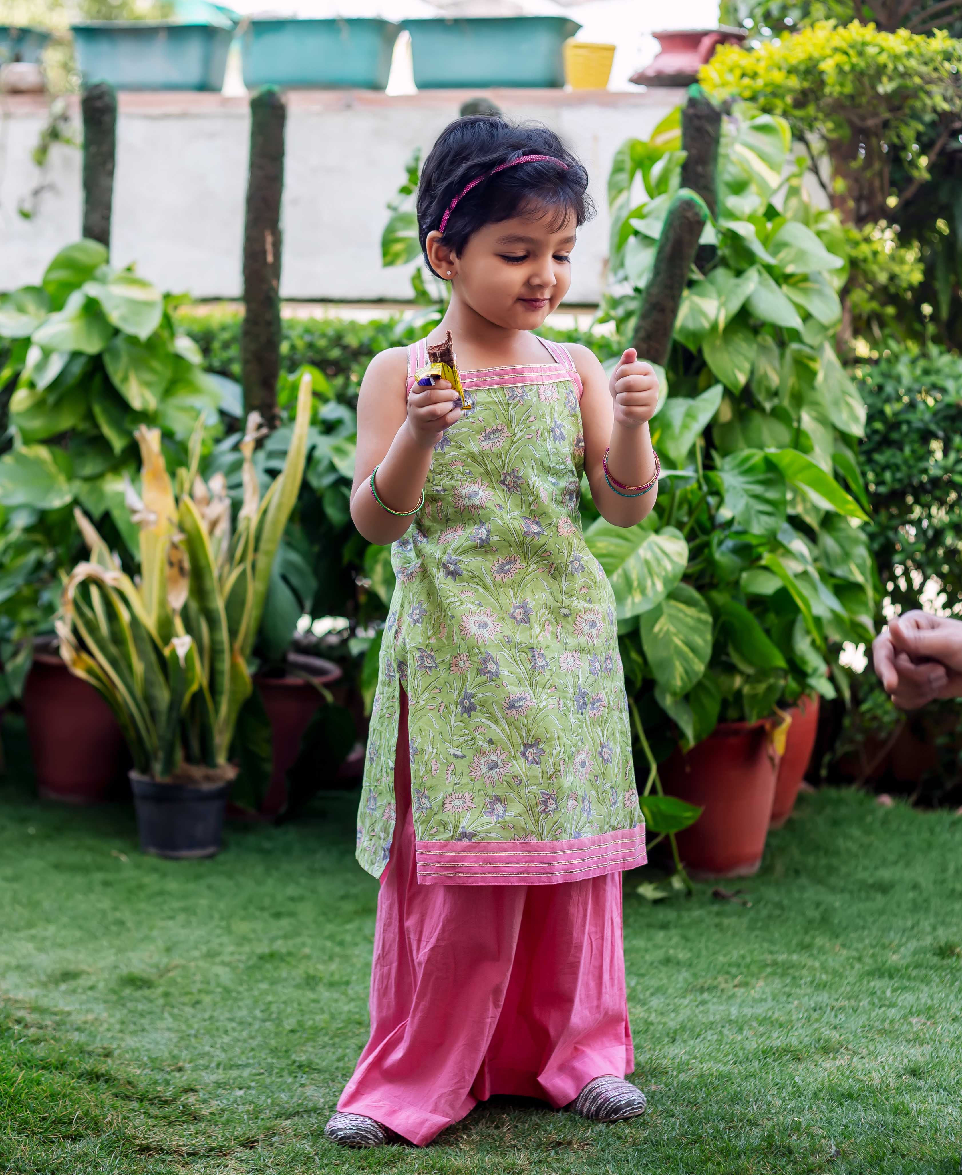 Front view of child in green hand-block printed kurta with pink trim and matching pink sharara.