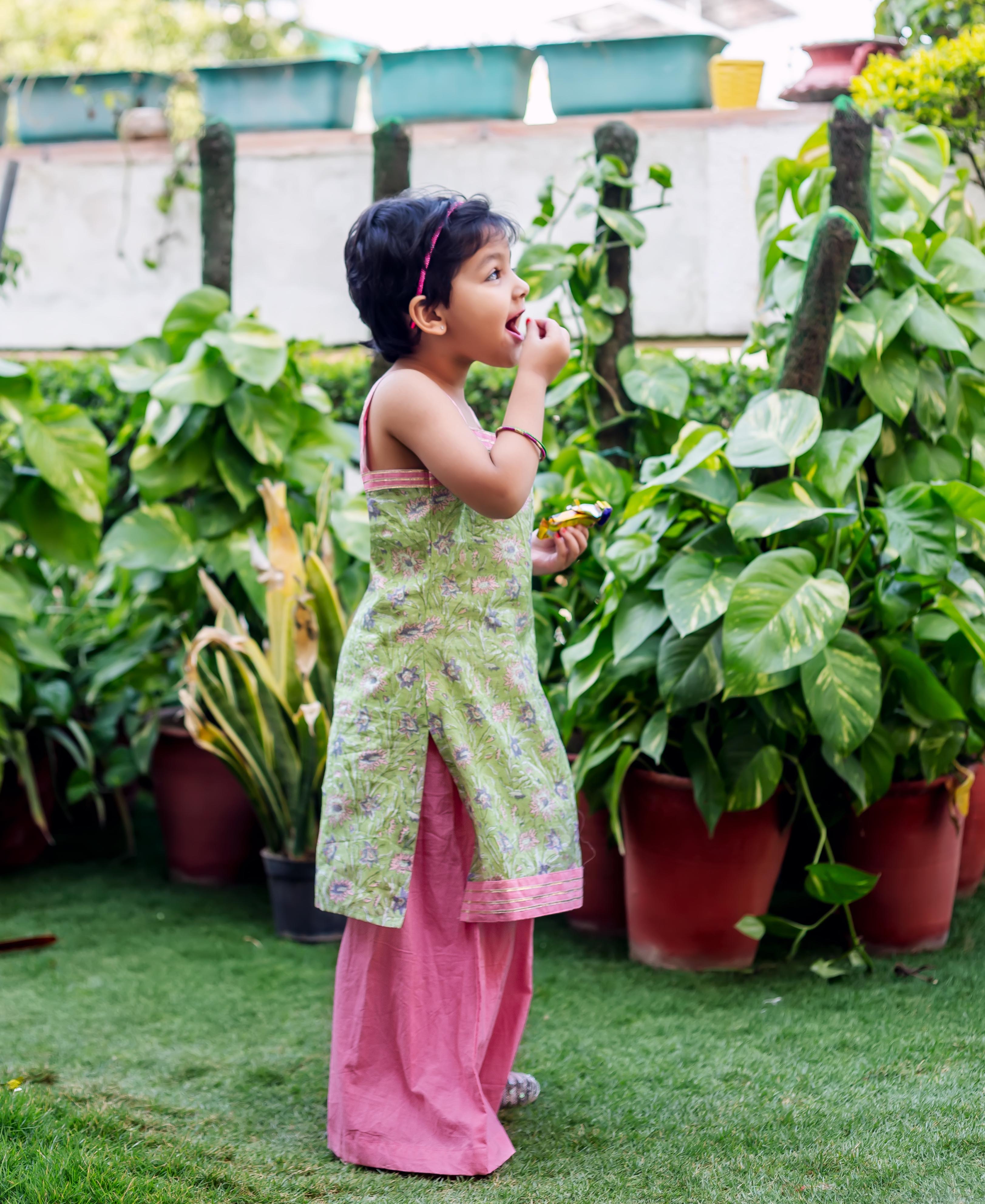 Child model in full-body side view, wearing a green hand-block-printed kurta and pink sharara.