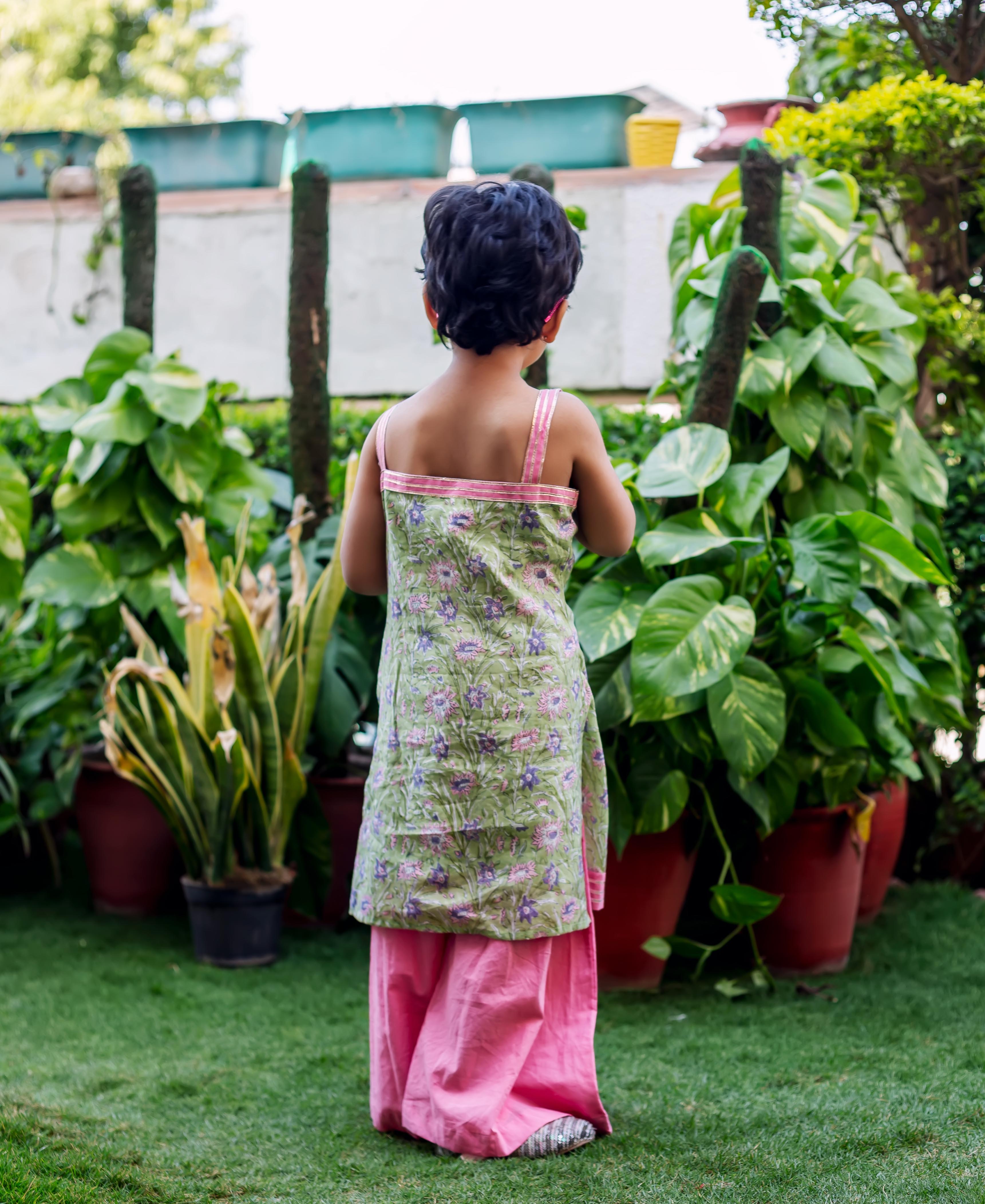Back view of child in green floral hand-block-printed kurta with pink sharara.