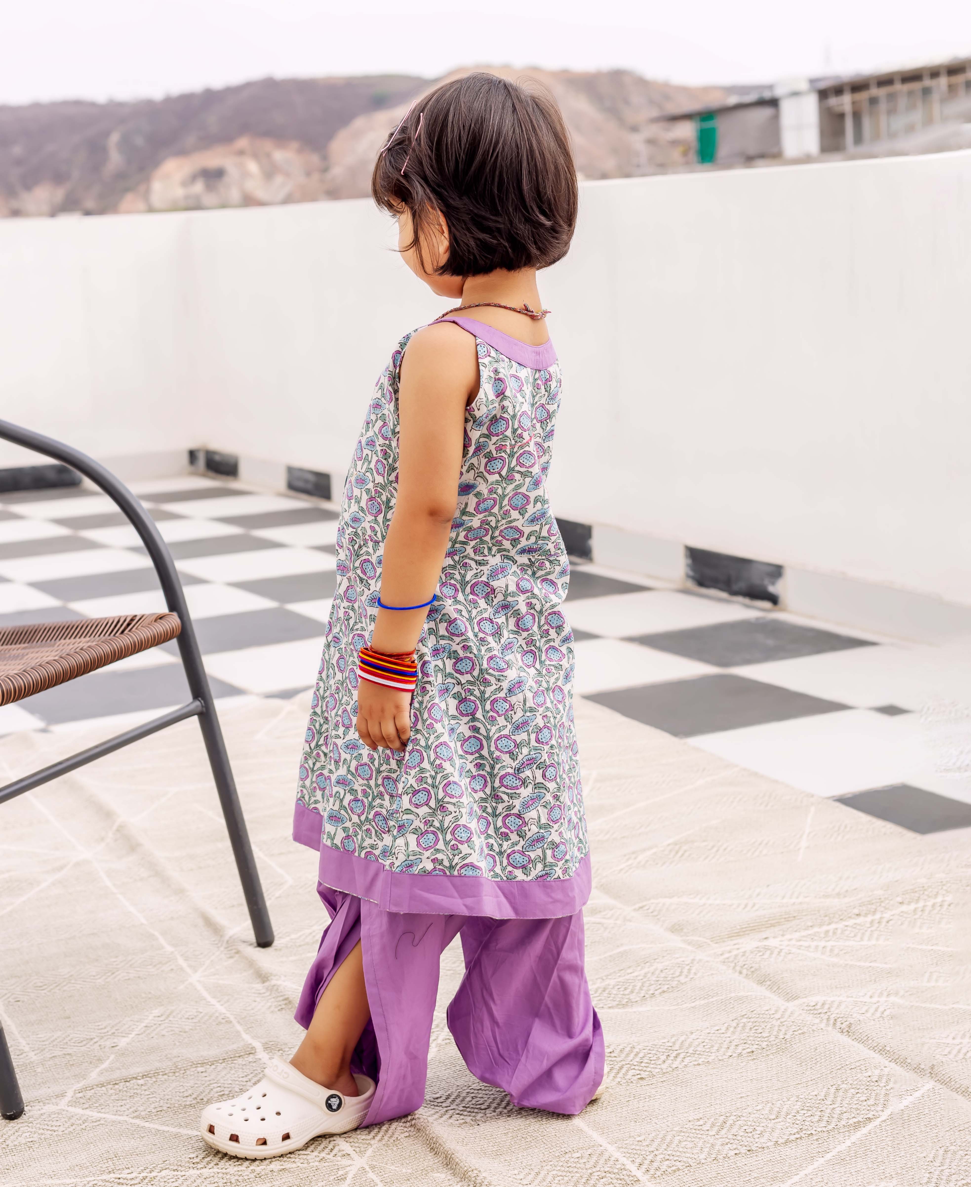 Young child from back, wearing white hand block printed purple floral kurta and purple dhoti.