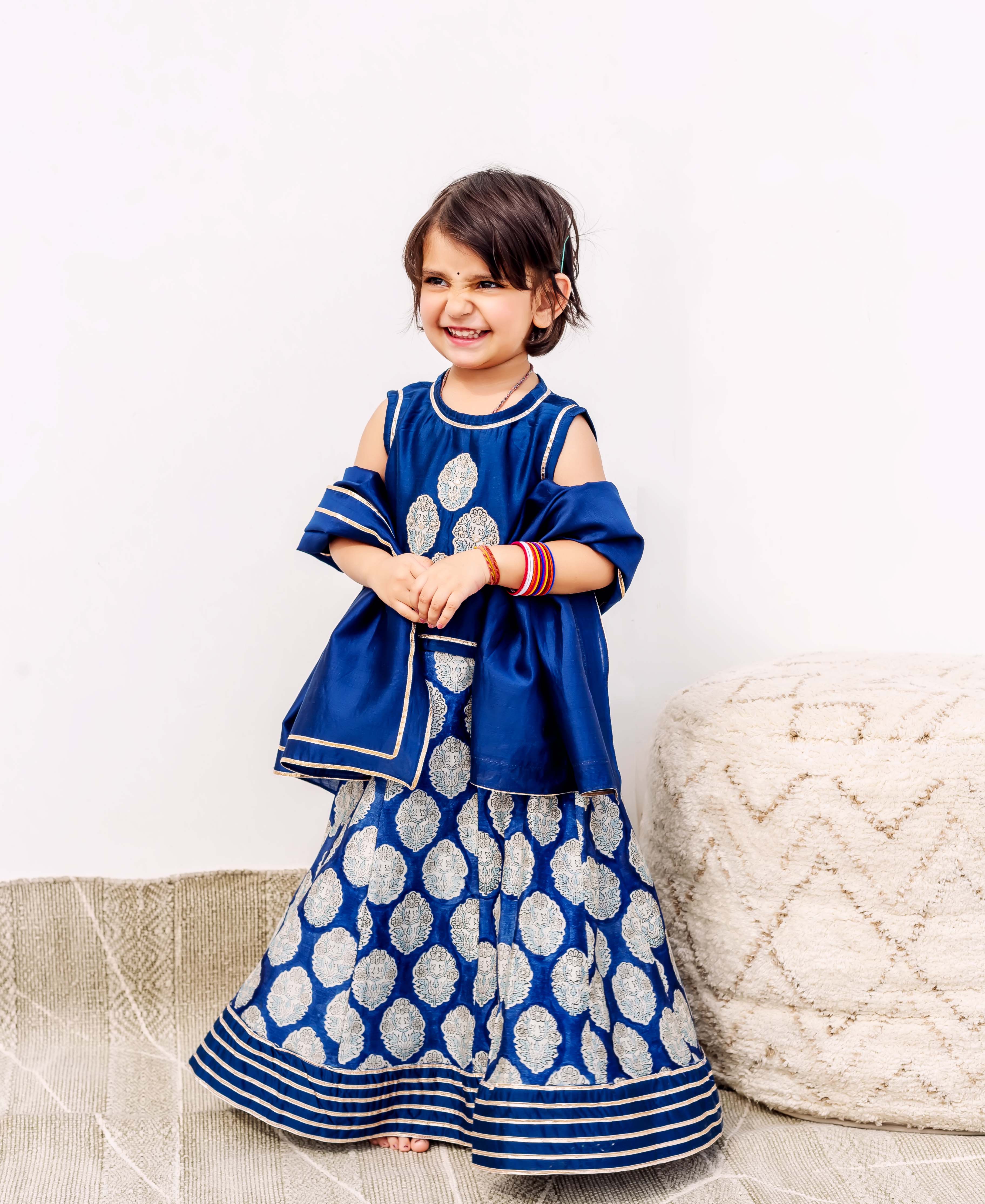 Child model in front-facing blue silk lehengha and cold-shoulder top with silver block print.
