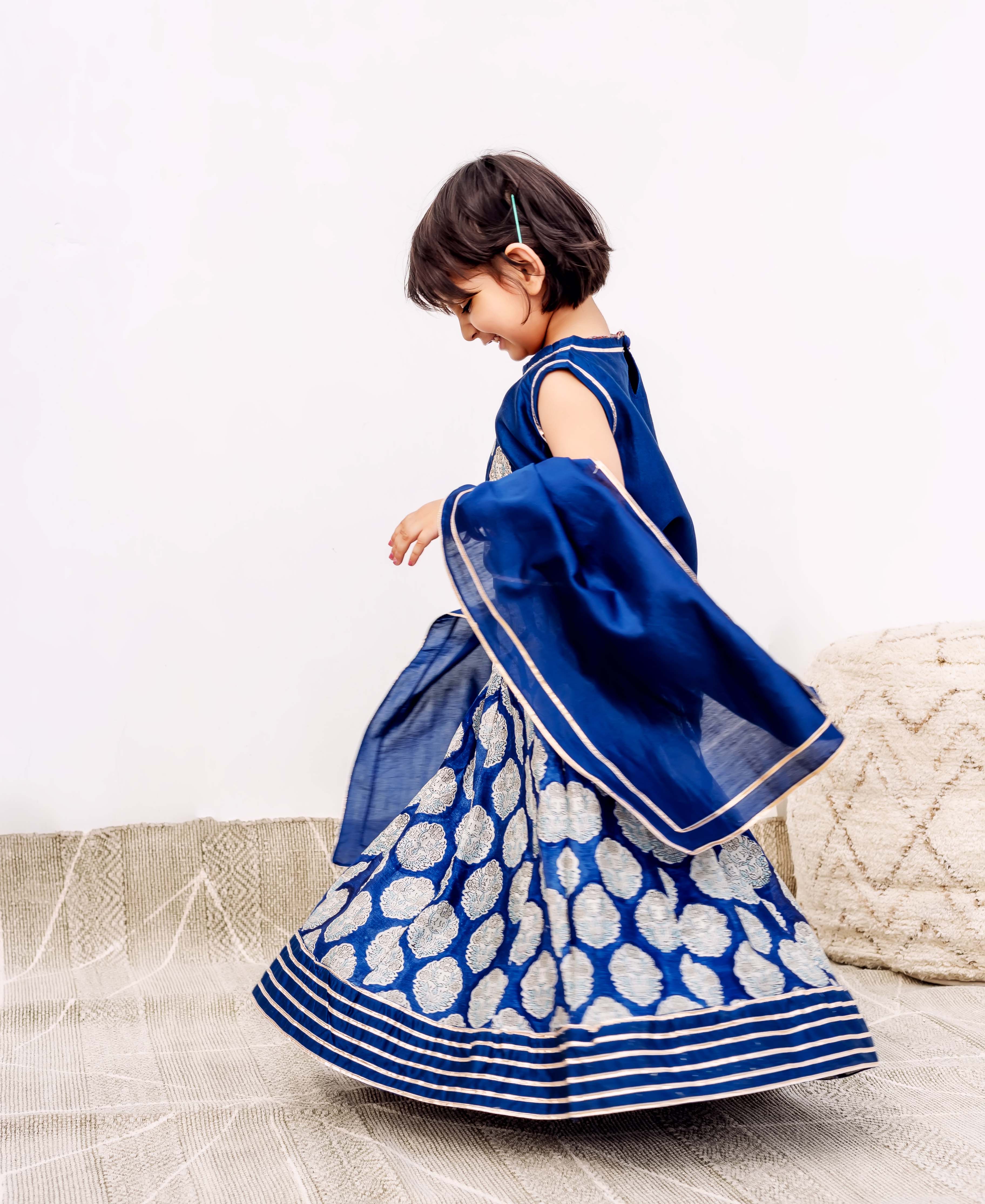 Young girl twirling in a blue hand-block printed silk lehenga with silver motifs and dupatta.