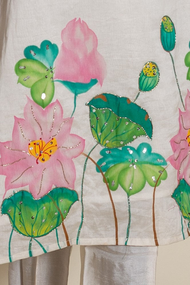 Close-up of ivory kurta with hand-painted pink lotus flowers, green leaves, and silver sequins.