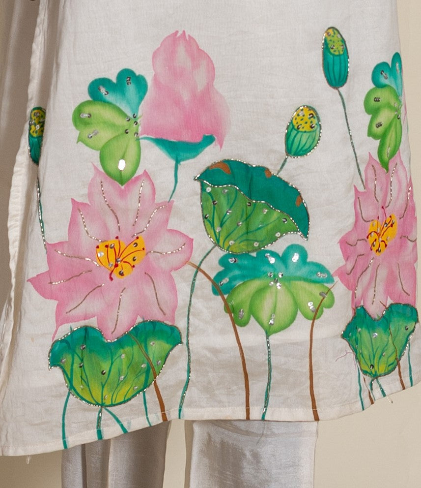 Close-up of ivory kurta with hand-painted pink lotus flowers, green leaves, and silver sequins.