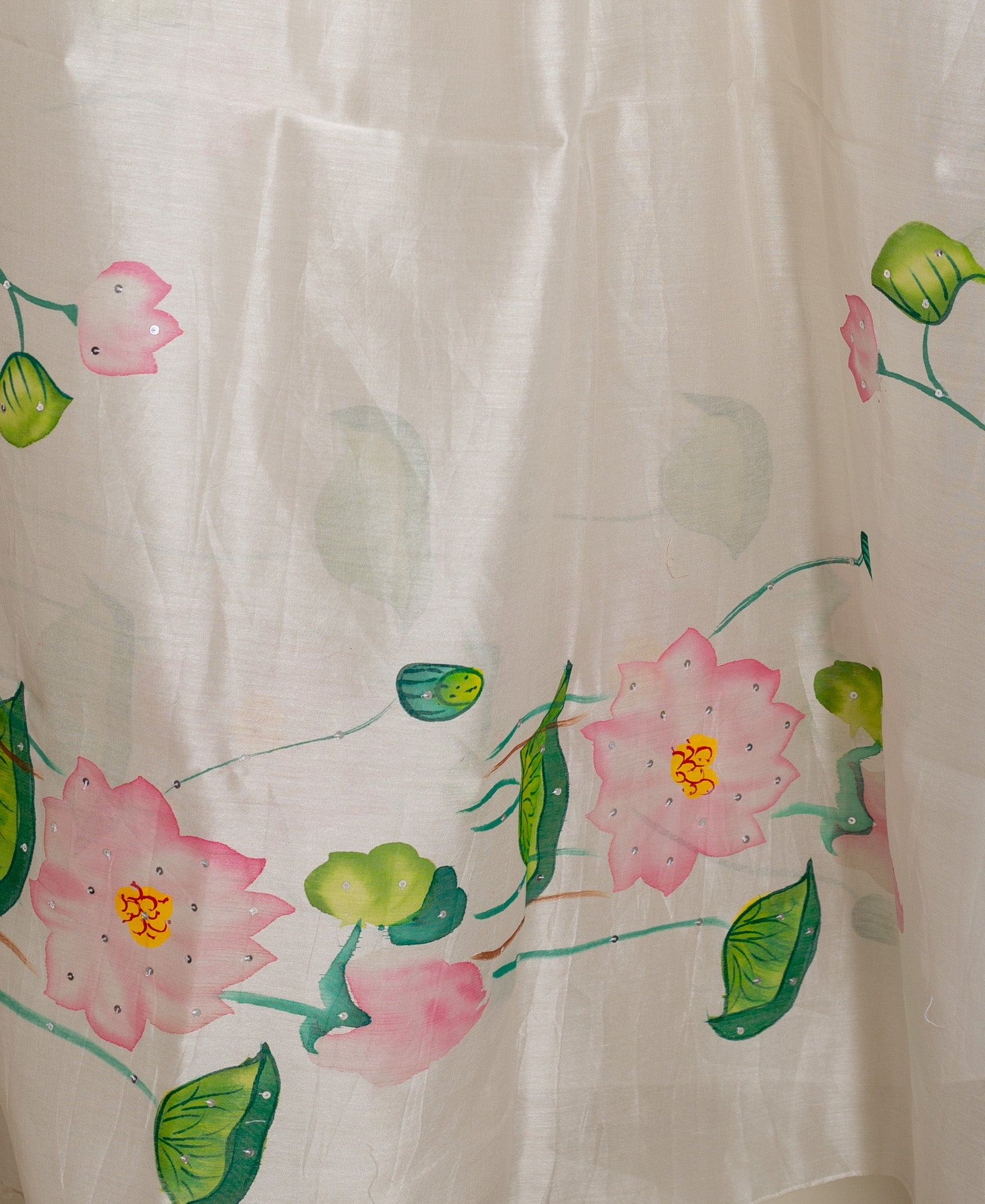 A close-up of a white, hand-painted floral kurta with pink lotus flowers and green leaves.