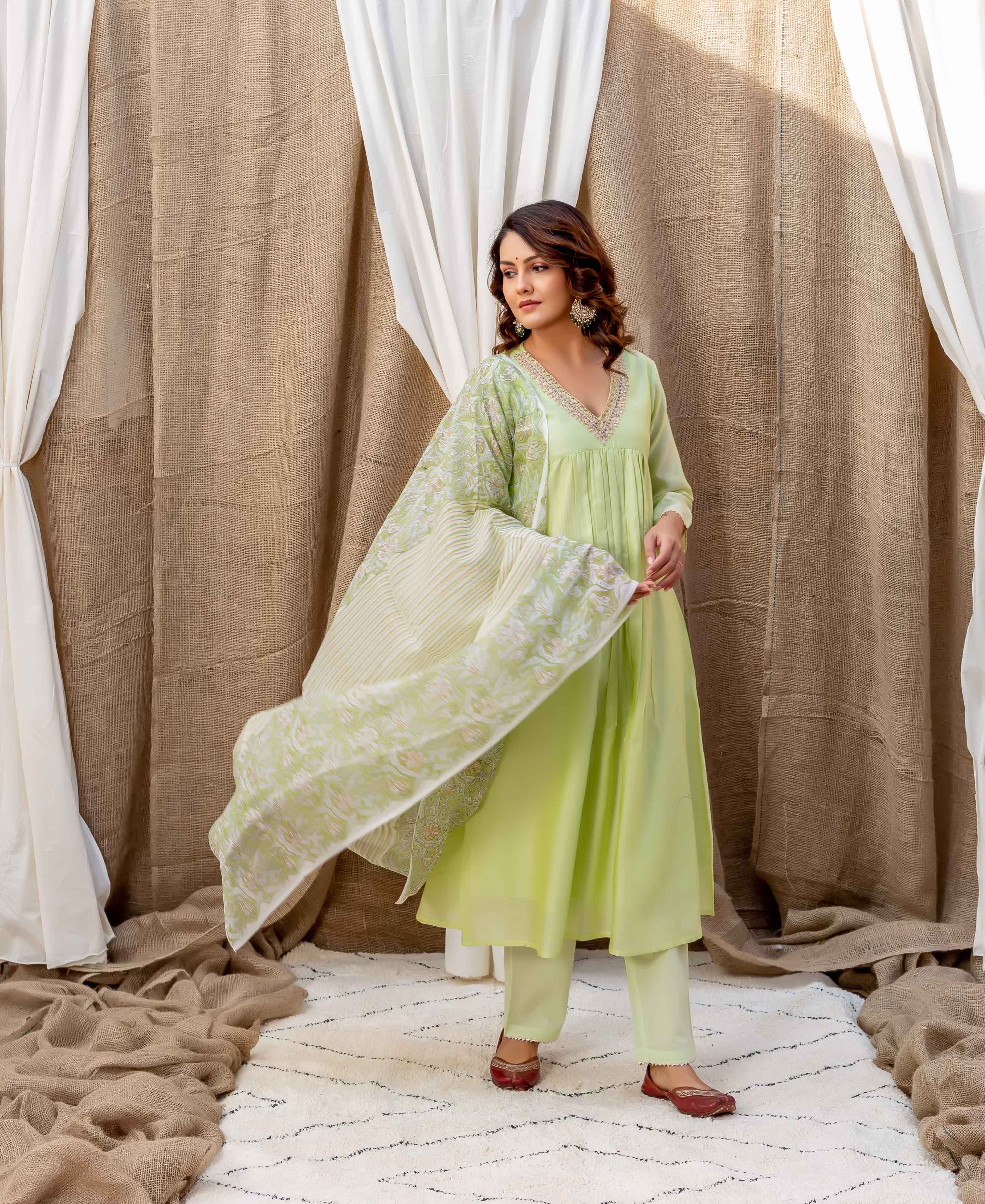 Woman in light green outfit with floral dupatta and embroidery, posing on white carpet.