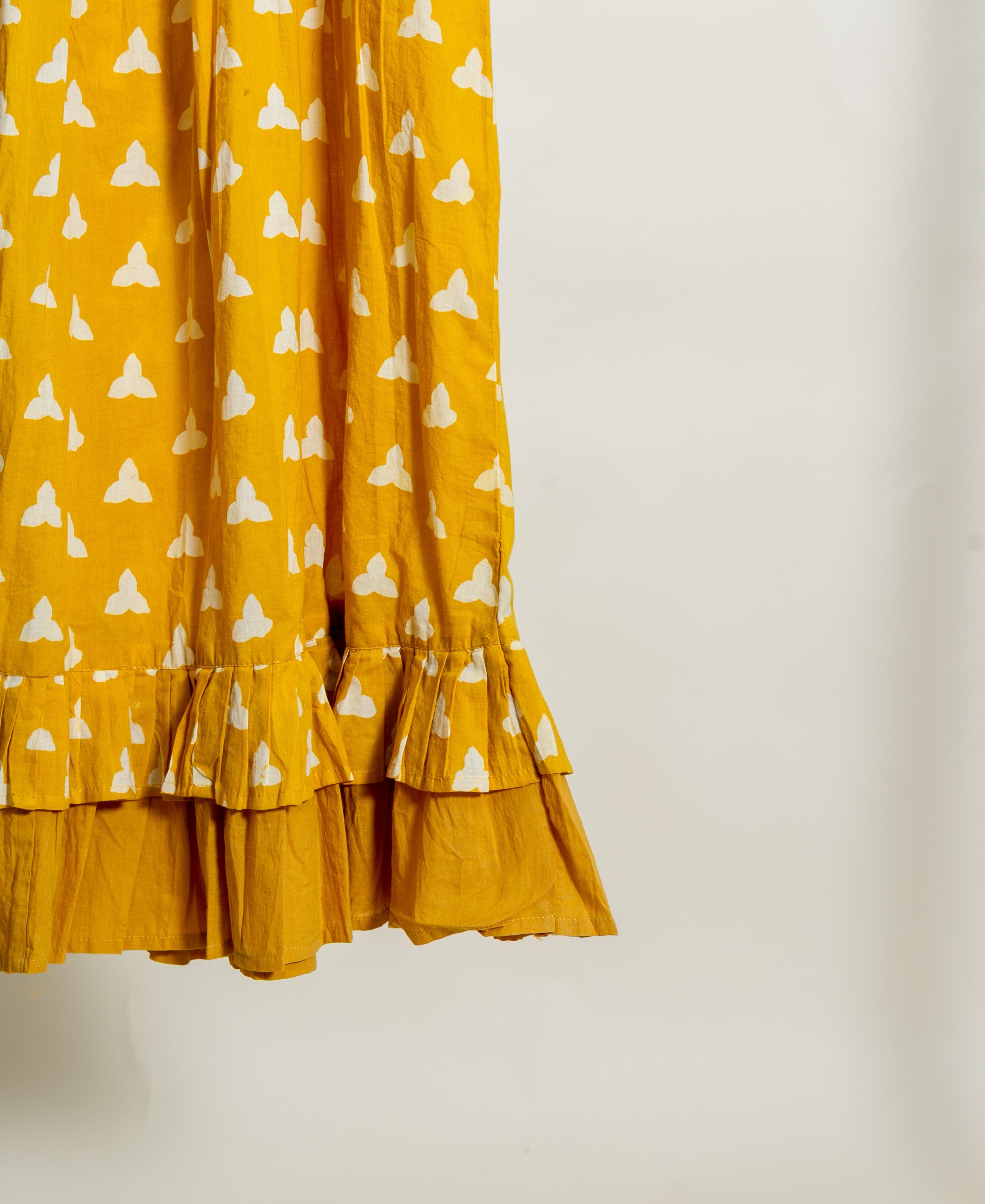 Yellow hand-block printed cotton dress featuring white patterns and a ruffled frill sweep.