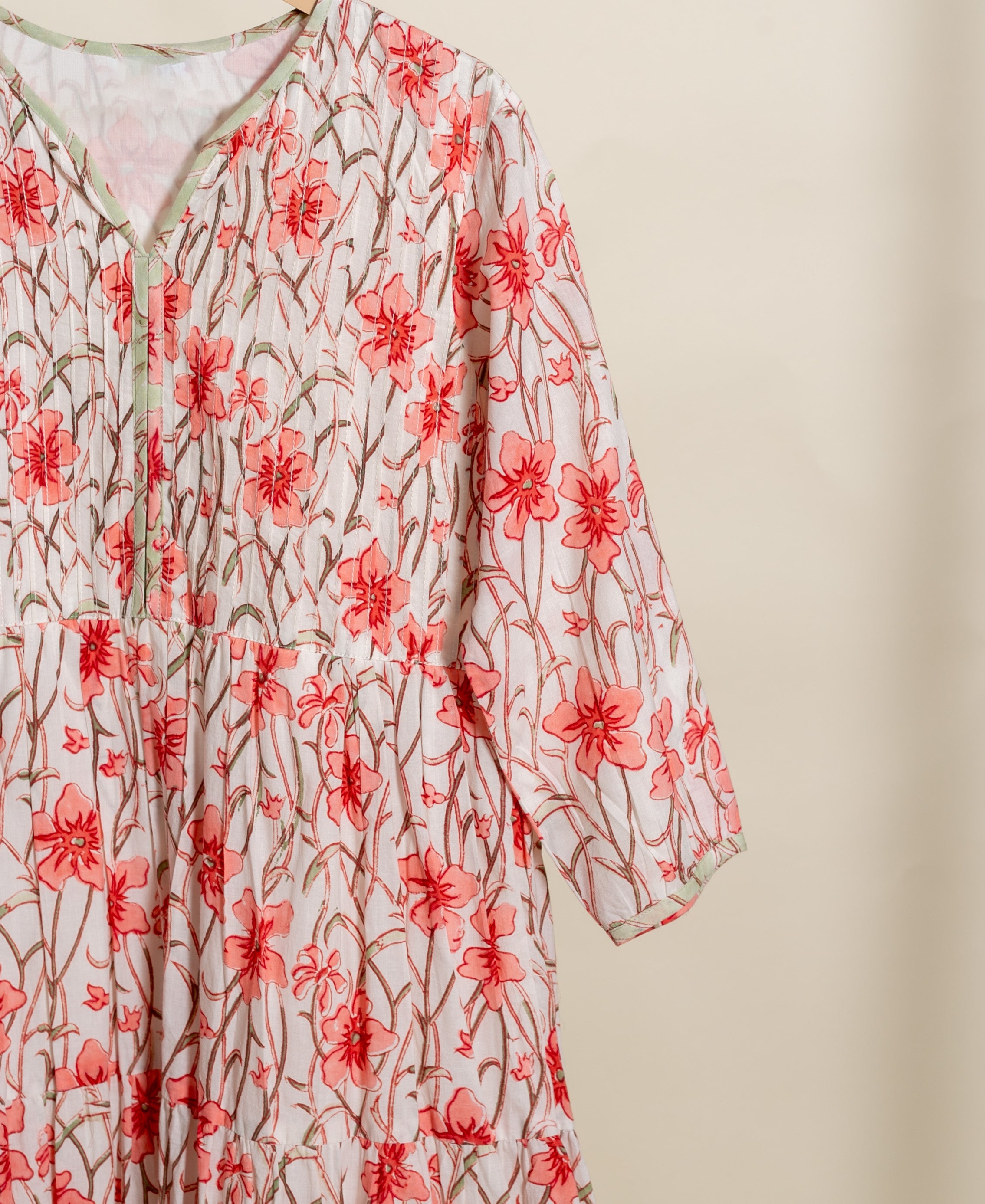 Close-up of white tiered cotton dress on hanger, V-neck, peach floral handblock print.
