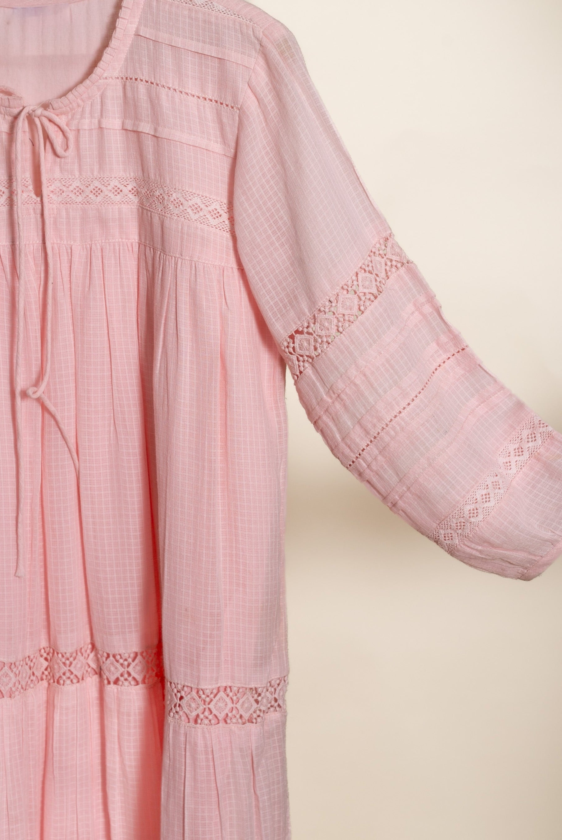 Pink checked dress with round tie-neck, lace-detailed sleeves, and tiered hem, shown flat.