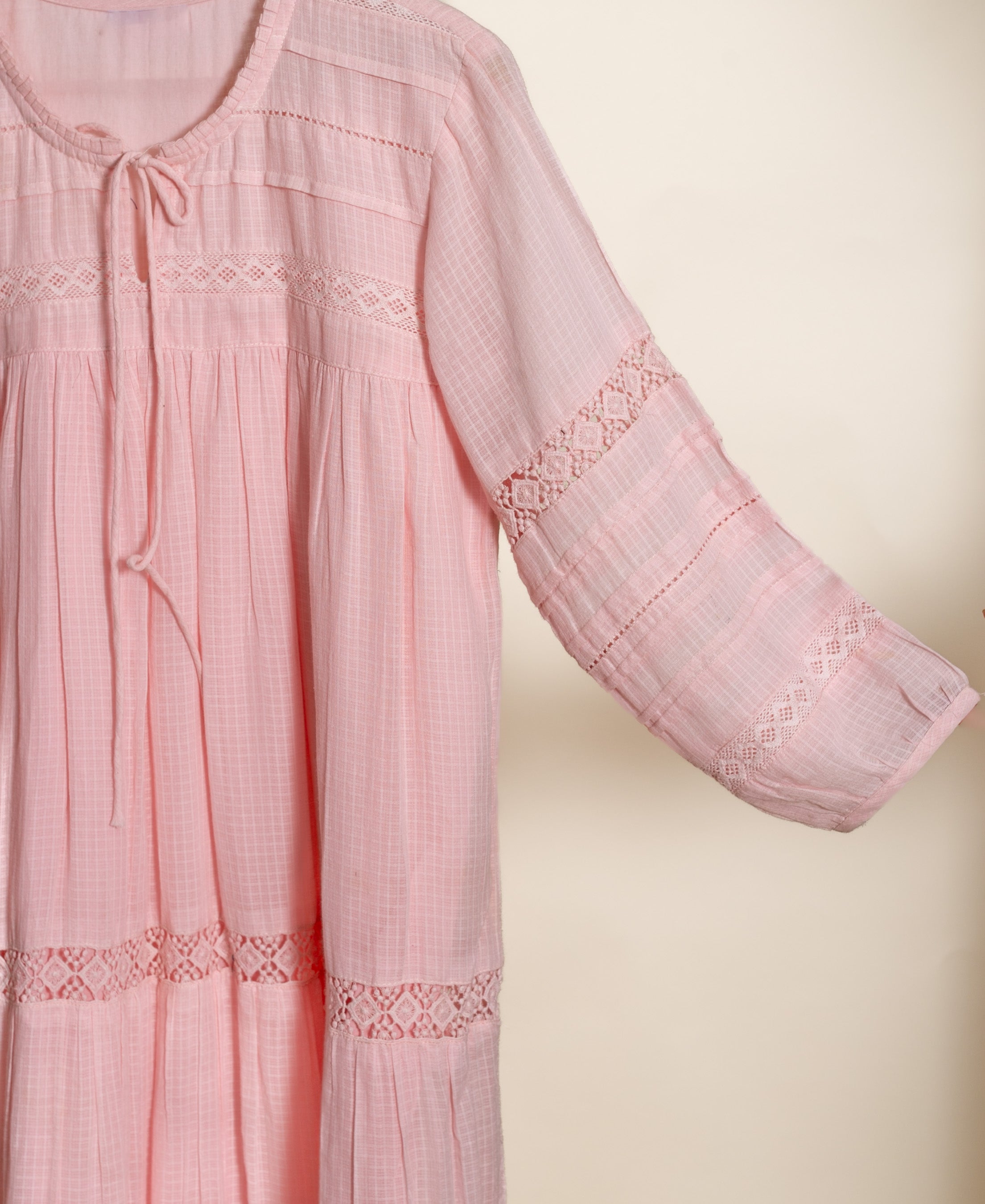 Pink checked dress with round tie-neck, lace-detailed sleeves, and tiered hem, shown flat.