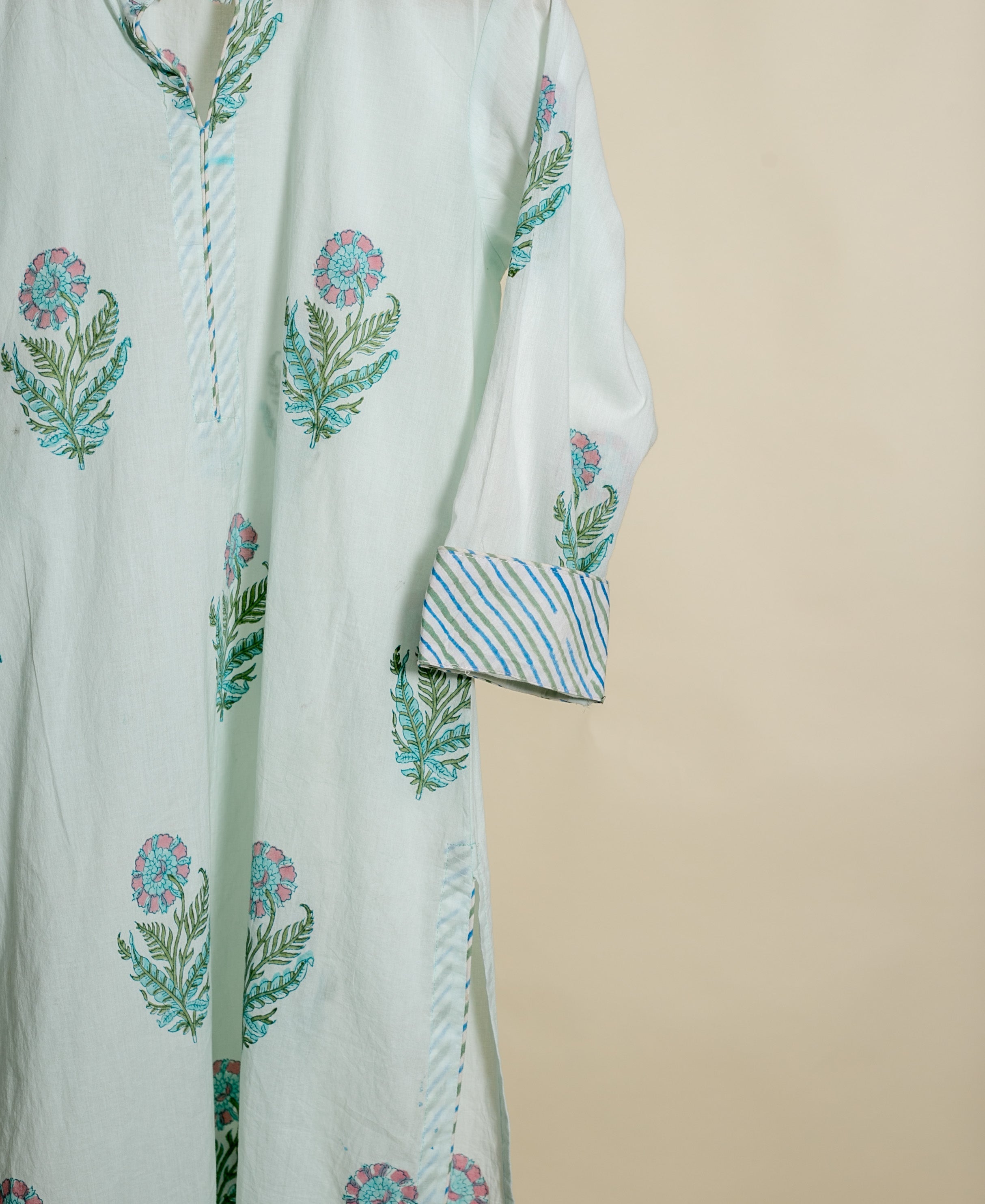 Angled view of a mint green handblock cotton kurta with pink botanical and blue striped patterns.