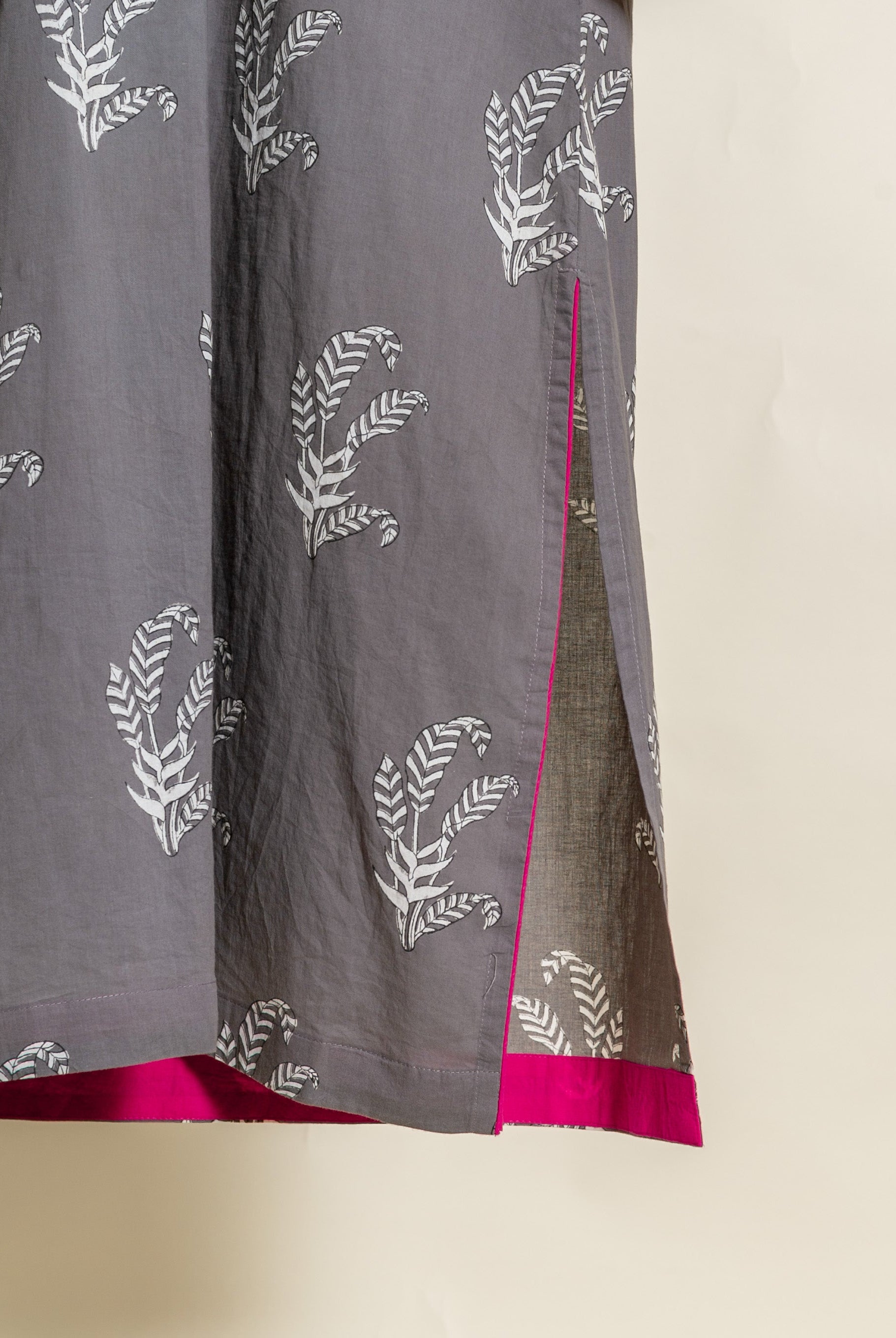 Close-up of grey hand-block cotton with white leaf print, featuring a pink-trimmed side slit and hem.