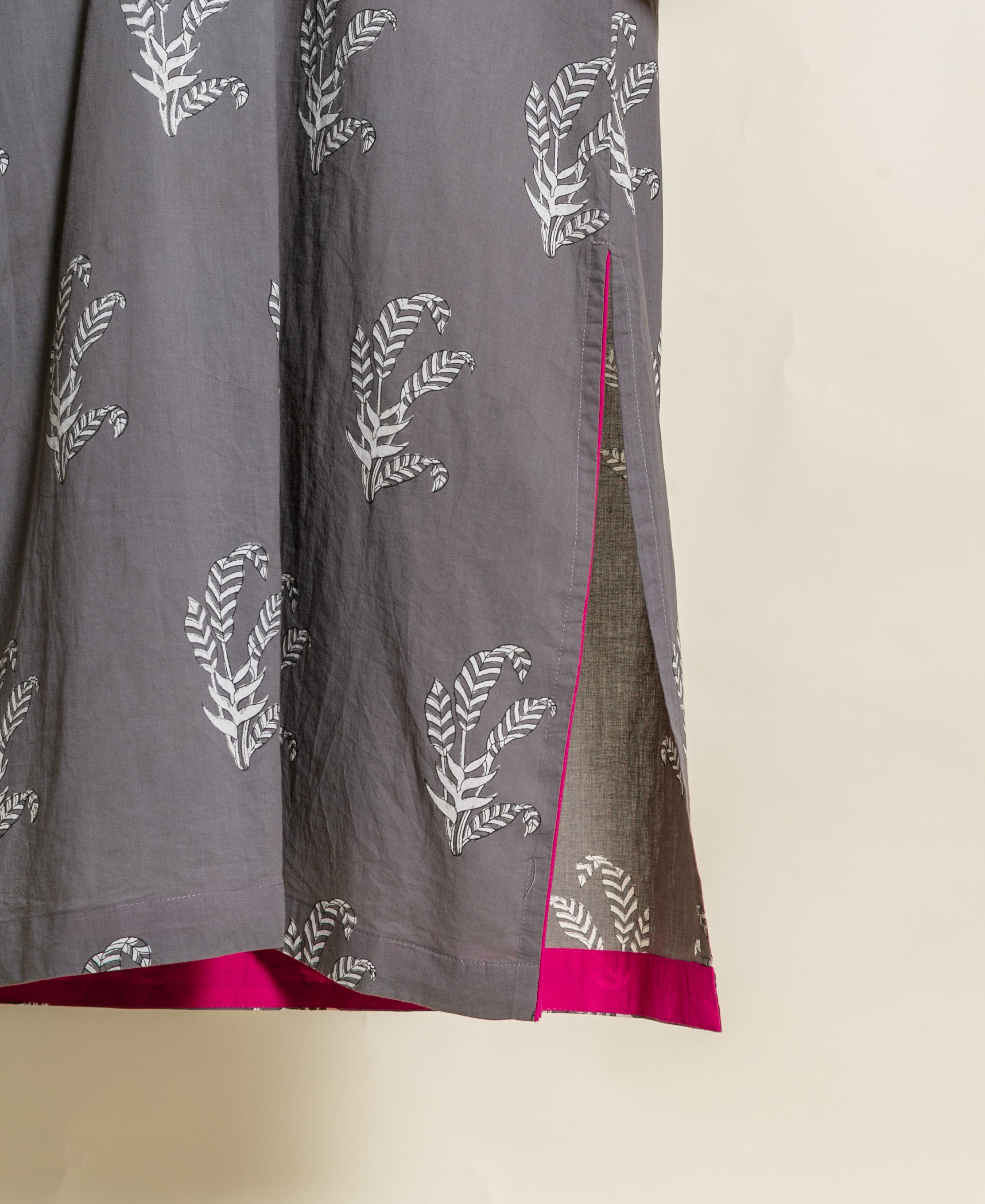 Close-up of grey hand-block cotton with white leaf print, featuring a pink-trimmed side slit and hem.