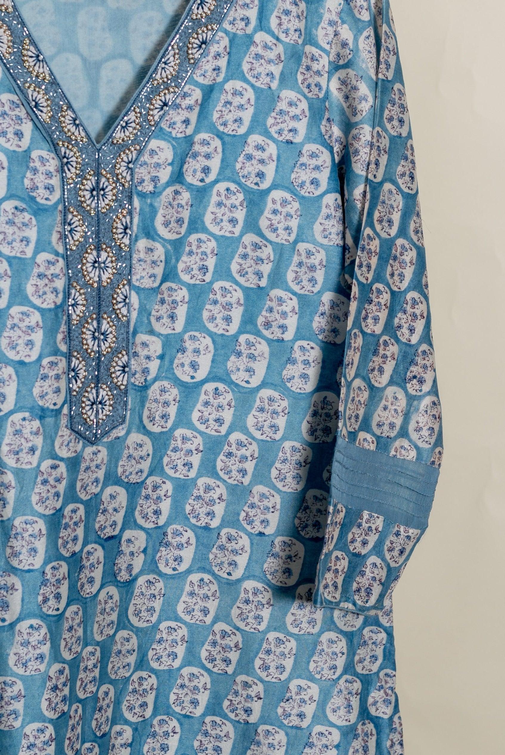 Dusty blue kurta with irregular white floral block print, beaded V-neck, and pleated sleeve.
