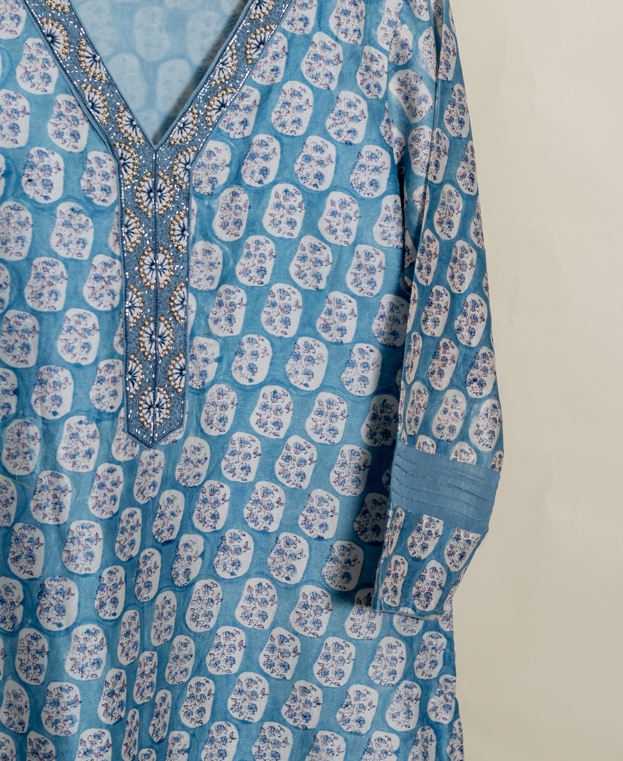 Dusty blue kurta with irregular white floral block print, beaded V-neck, and pleated sleeve.