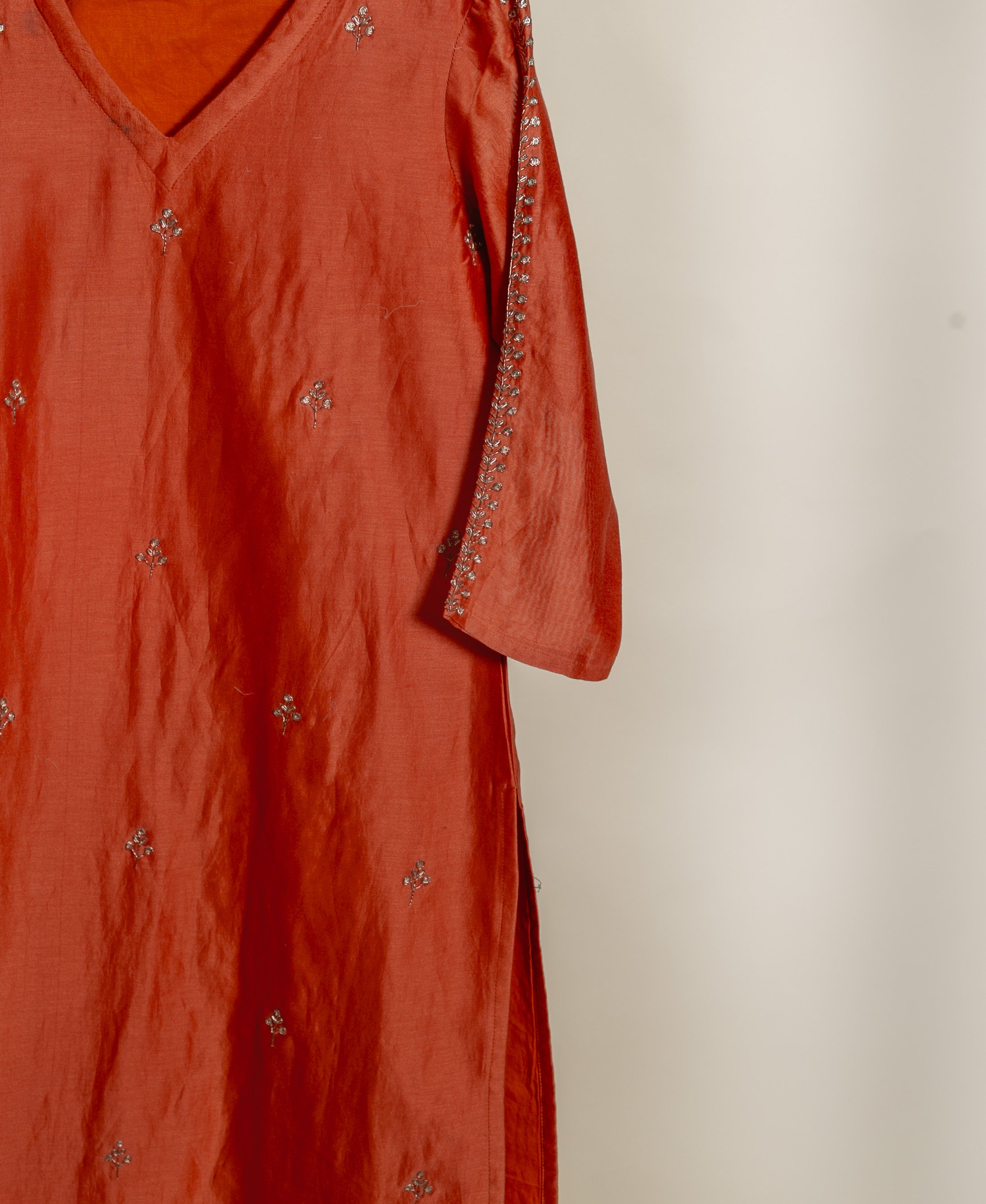 Rust V-neck kurta with scattered silver embroidery and embellished sleeves, shown hanging.