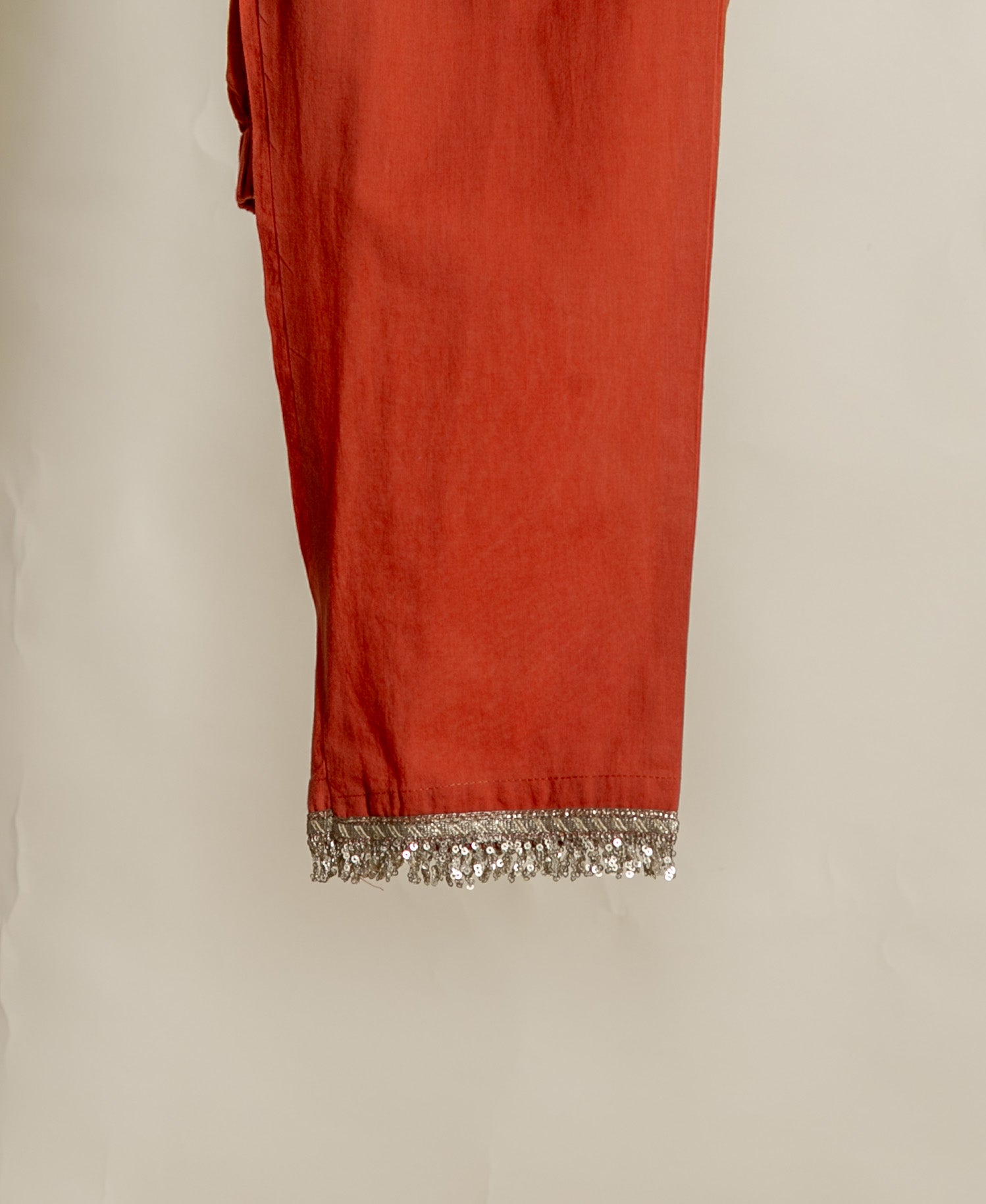 Flat lay close-up of rust-coloured pants with a silver sequin-embellished fringed hem.
