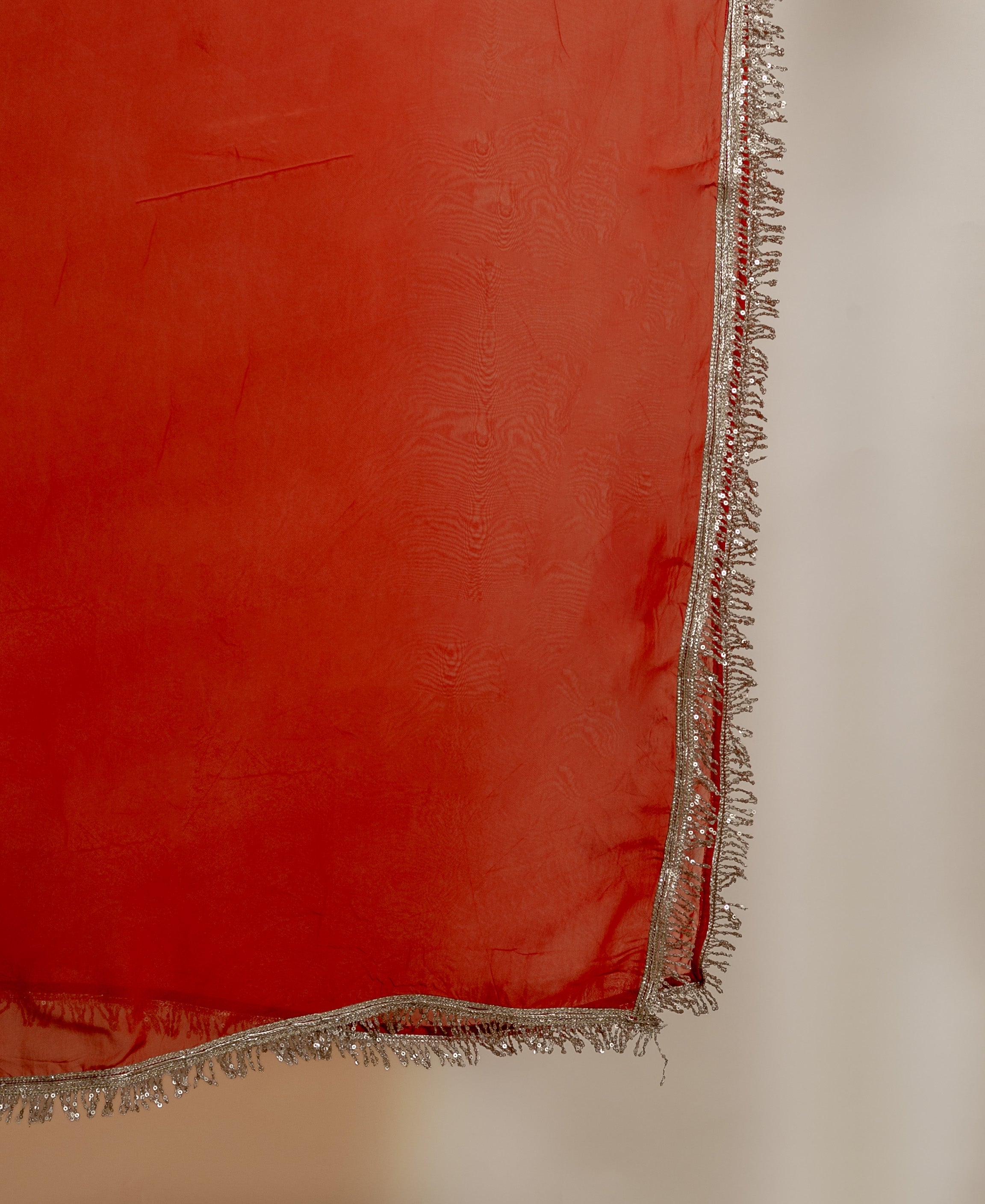 Close-up of rust-colored draped silk fabric with a silver sequin and bead border.