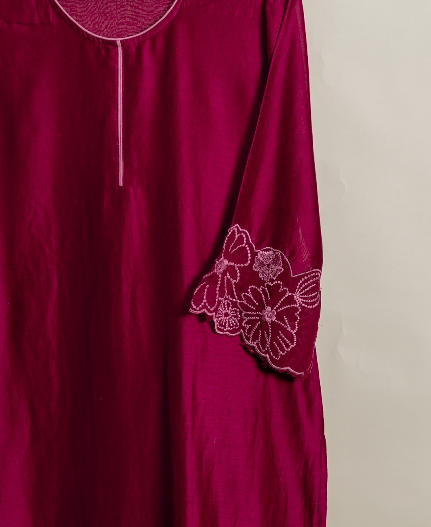 Hanging deep magenta kurta with light pink stitched placket and floral embroidery on the sleeve.