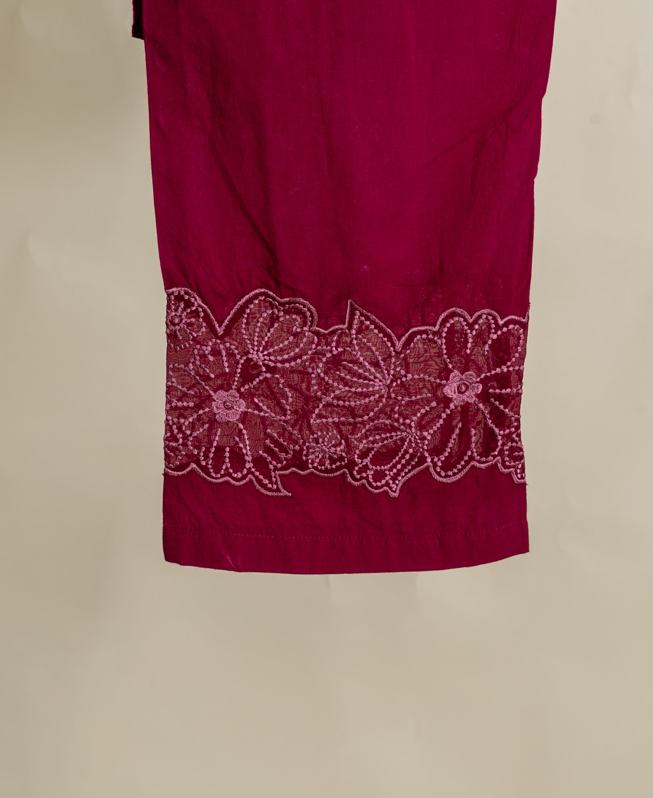 Close-up flat lay of wine red garment with intricate pink floral embroidery at the hem.
