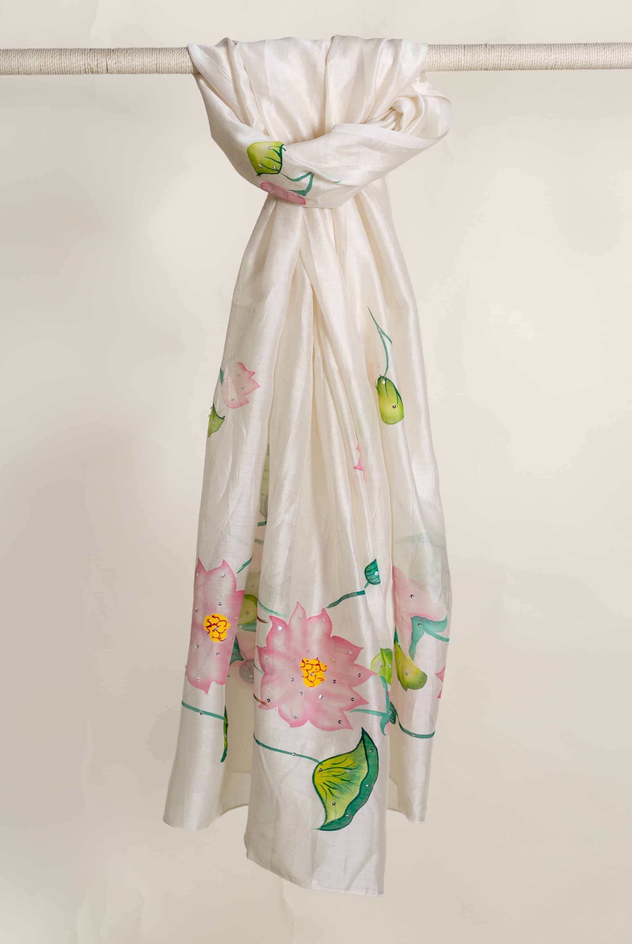 Ivory hand-painted silk dupatta featuring sparkling pink lotus flowers and green leaves, hanging.