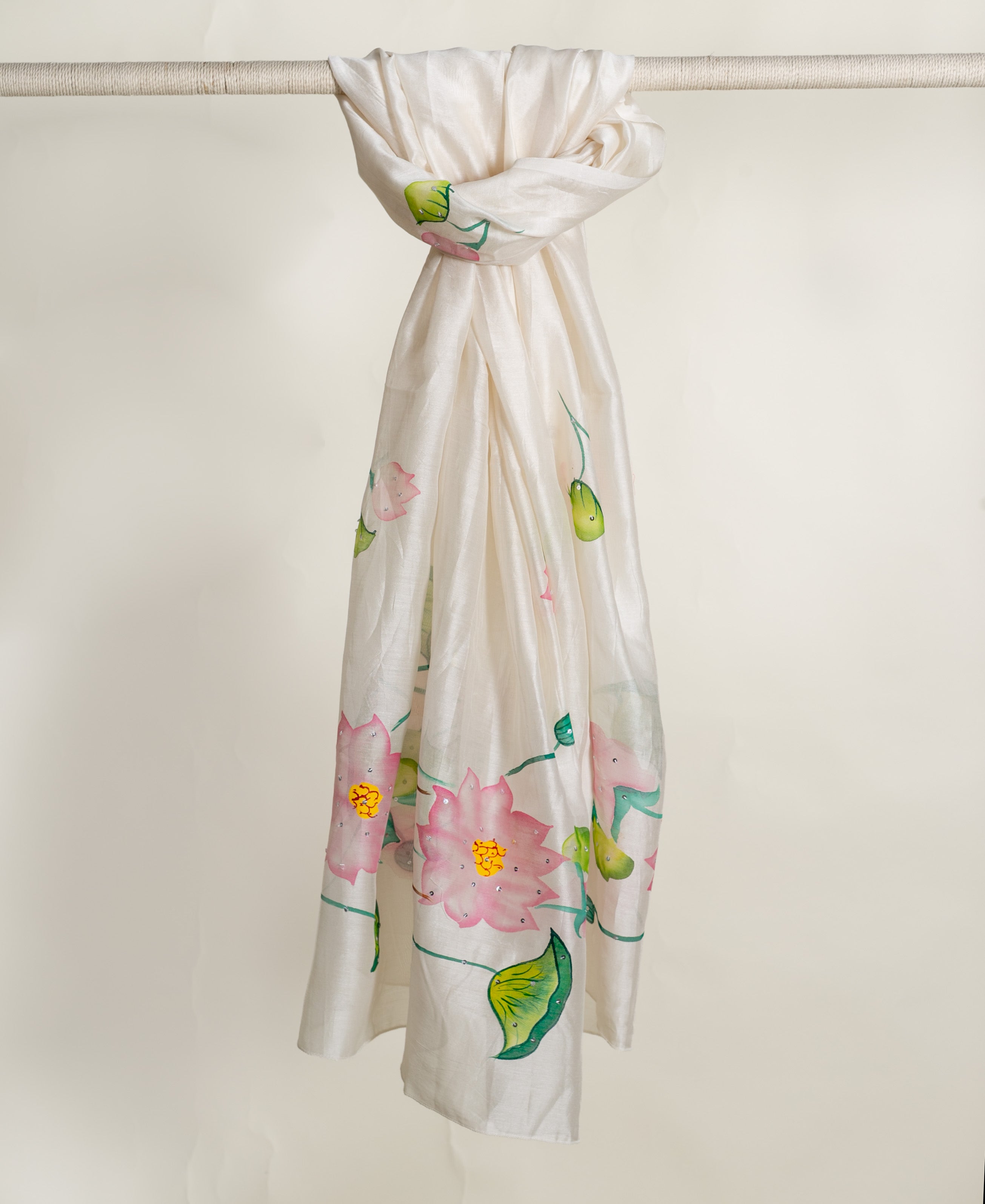 Ivory hand-painted silk dupatta featuring sparkling pink lotus flowers and green leaves, hanging.