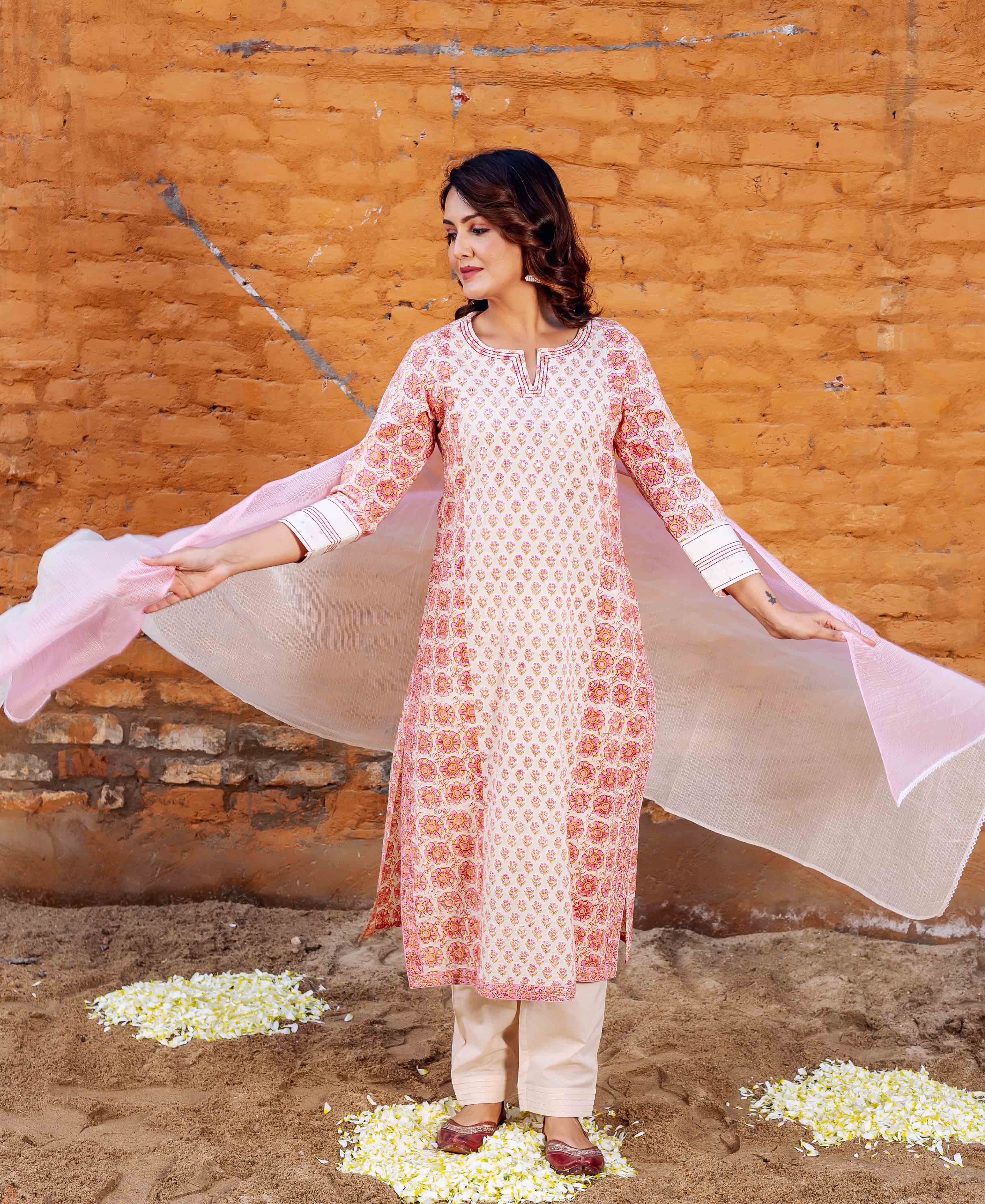 Woman in long pink and white block printed cotton kurta with floral pattern and beige trousers.